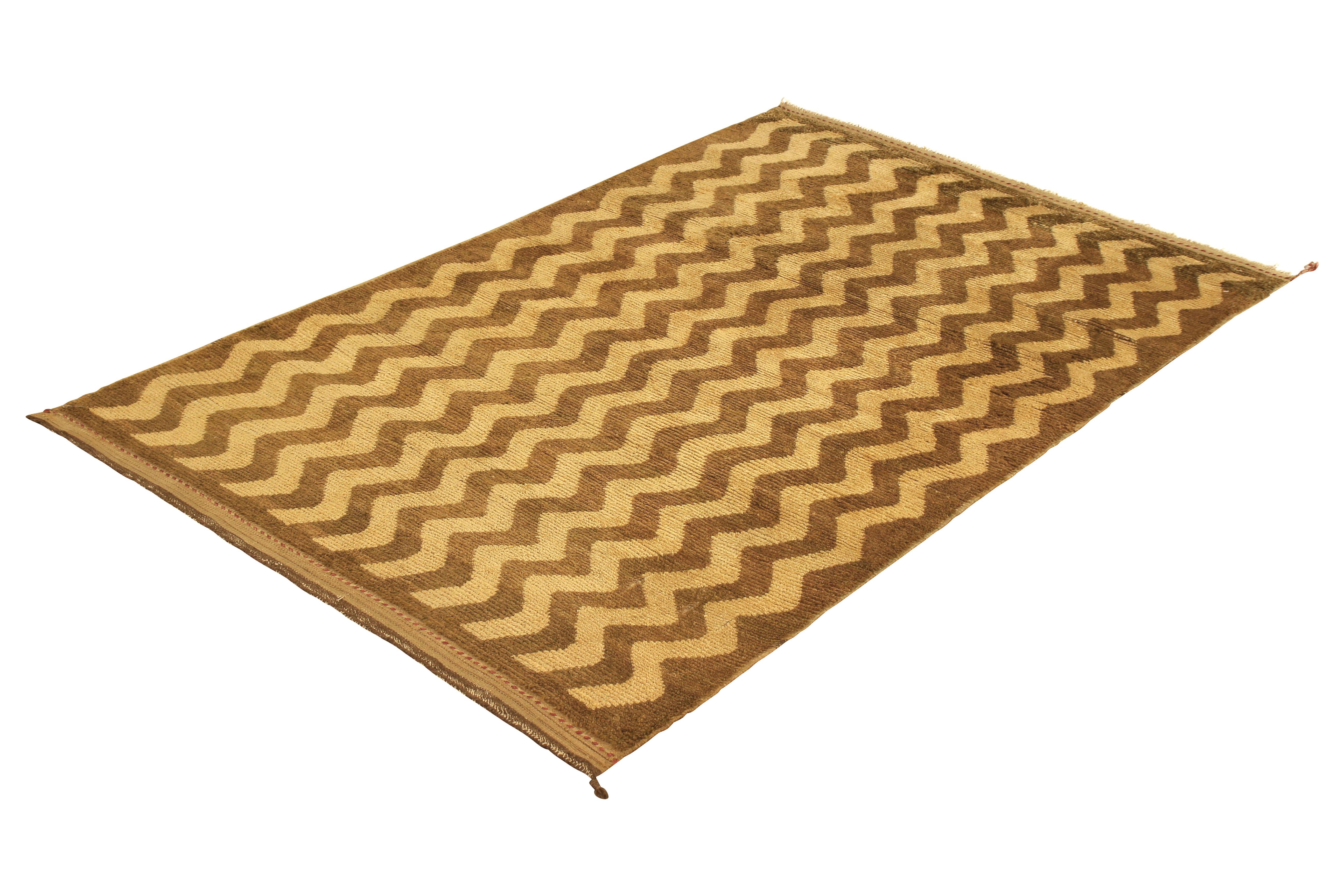 Hand knotted in wool originating from Turkey, circa 1950-1960, this vintage rug connotes a midcentury Tulu rug design, enjoying an idyllic Classic play of zig-zag chevron striped patterns with rich notes of brown and beige/camel colorway tones.