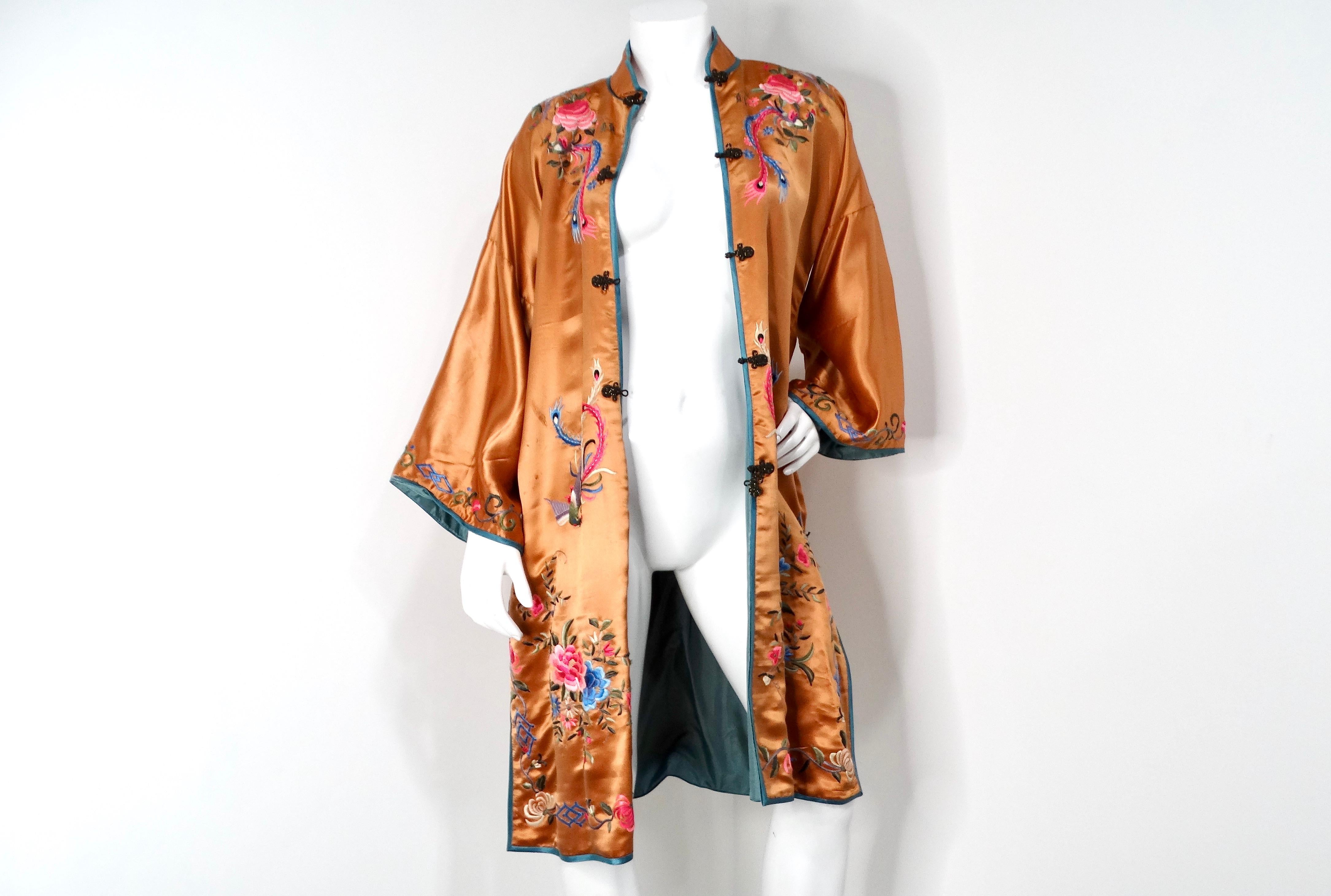 This stunning 1950s vintage orange Chinese silk floral embroidered print jacket is a timeless piece that beautifully encapsulates the elegance of mid-century fashion. Crafted from 100% luxurious silk, its vibrant orange hue serves as an eye-catching