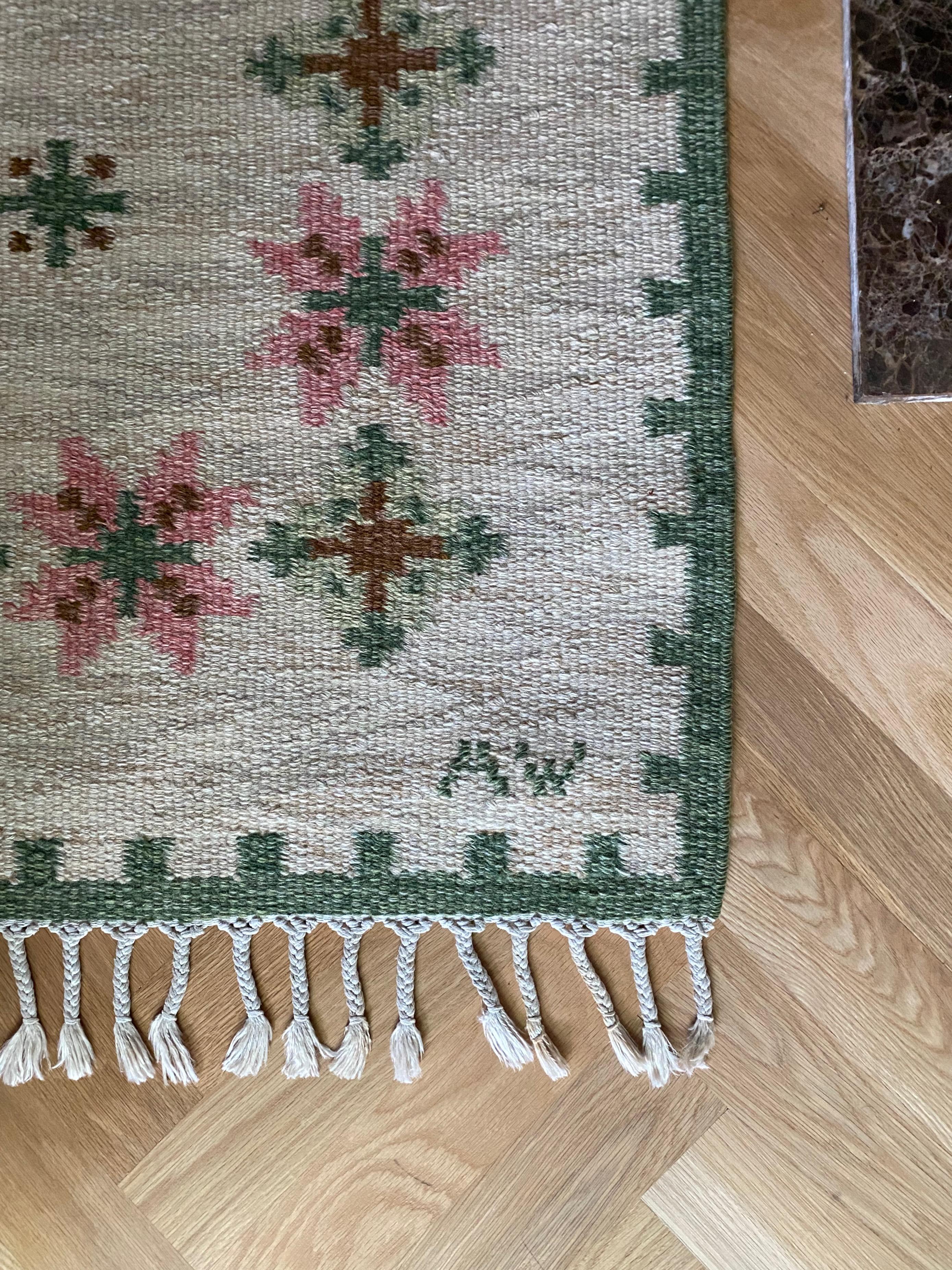 Vintage Swedish Kilim by Alice Wallebäck in white, green and pink colors. Geometric flower motif with a green border along the edges. Designer initial AW in right corner. Very good vintage condition.

Country: Sweden

Maker: Alice
