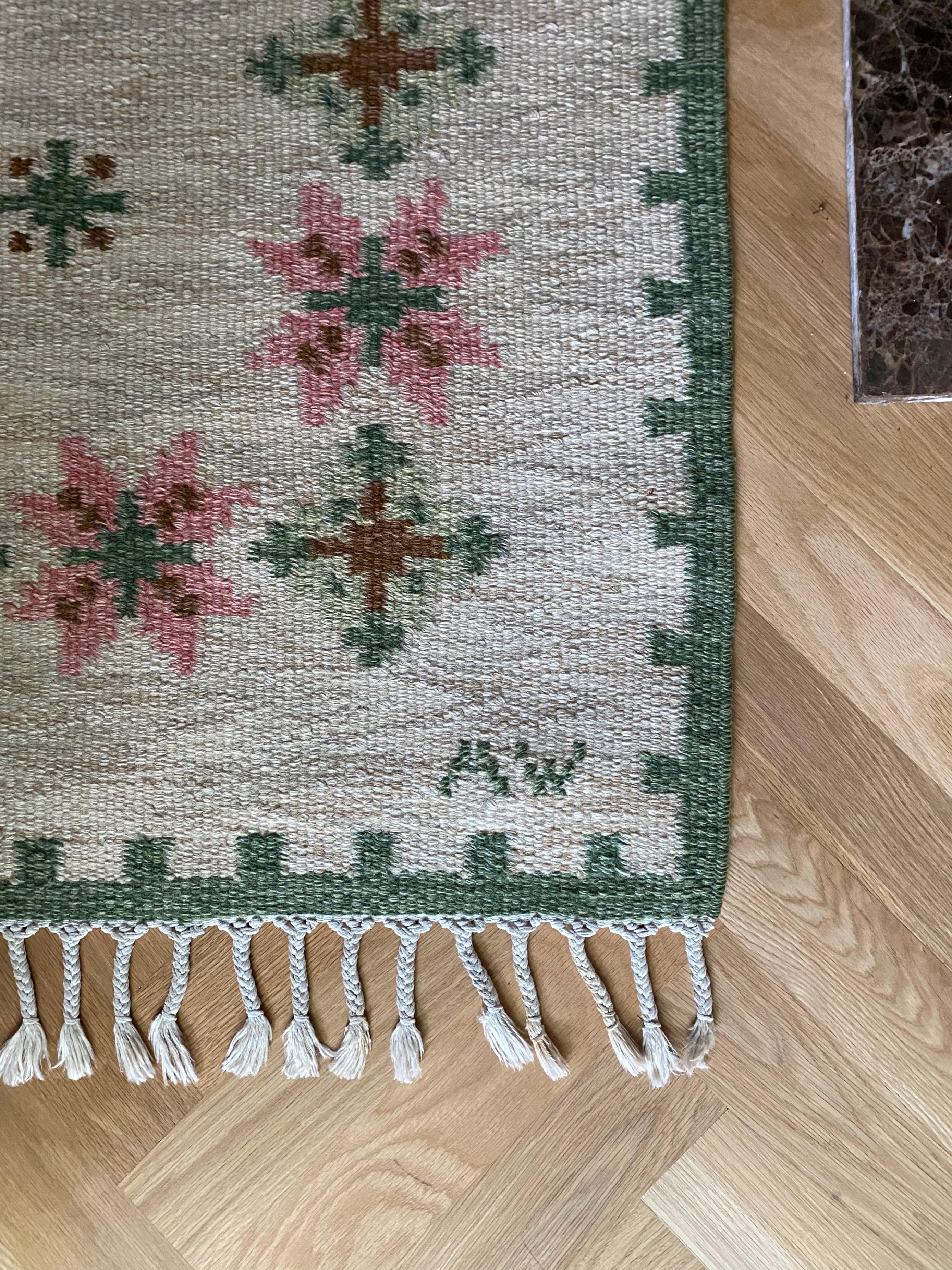 Vintage Swedish Kilim by Alice Wallebäck in white, green and pink colors. Geometric flower motif with a green border along the edges. Designer initial AW in right corner. Very good vintage condition.

Country: Sweden

Maker: Alice