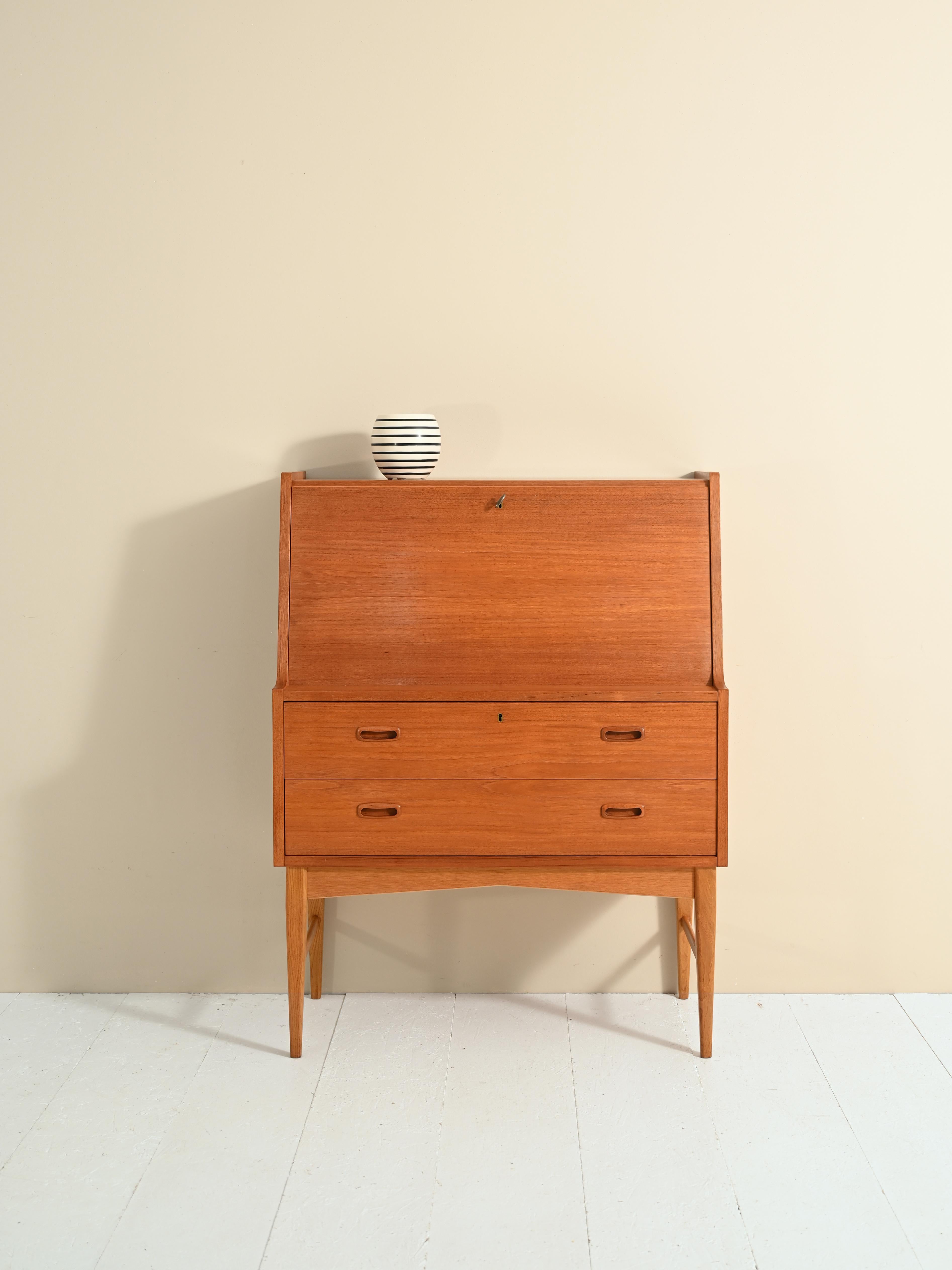 Teak cabinet with drawers and flap. 

The front can be opened if needed and become a convenient desk. Inside are shelves, a drawer and a mirror hidden behind a door. 

At the bottom of the cabinet are two large drawers with a carved wooden