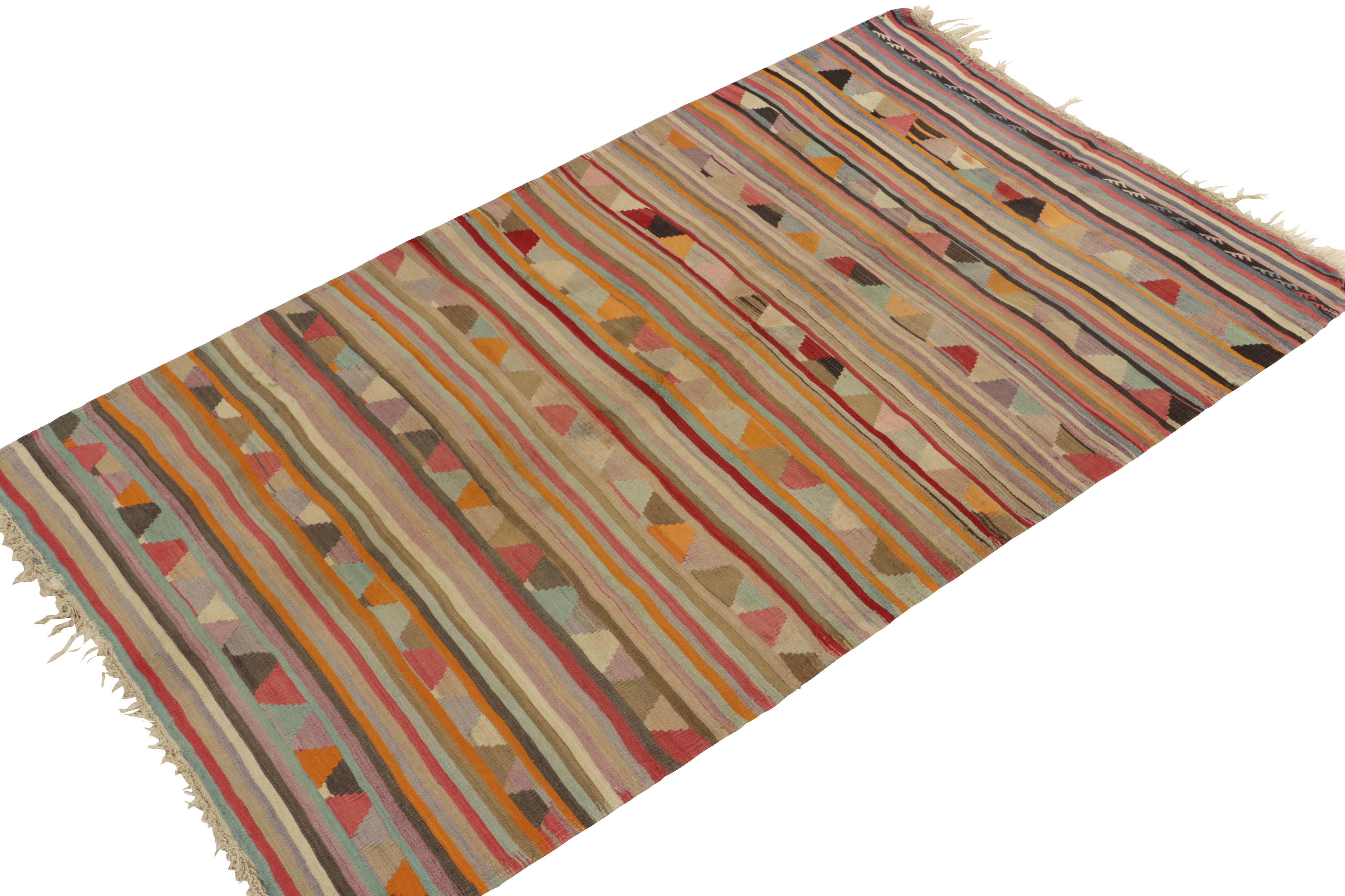 Hailing from Turkey circa 1950-1960, a 5x9 vintage kilim from Rug & Kilim’s most coveted mid-century curations. This particular rug plays a striped background with the most unusual, vibrant geometric patterns in gold-orange, pink, blue, and other