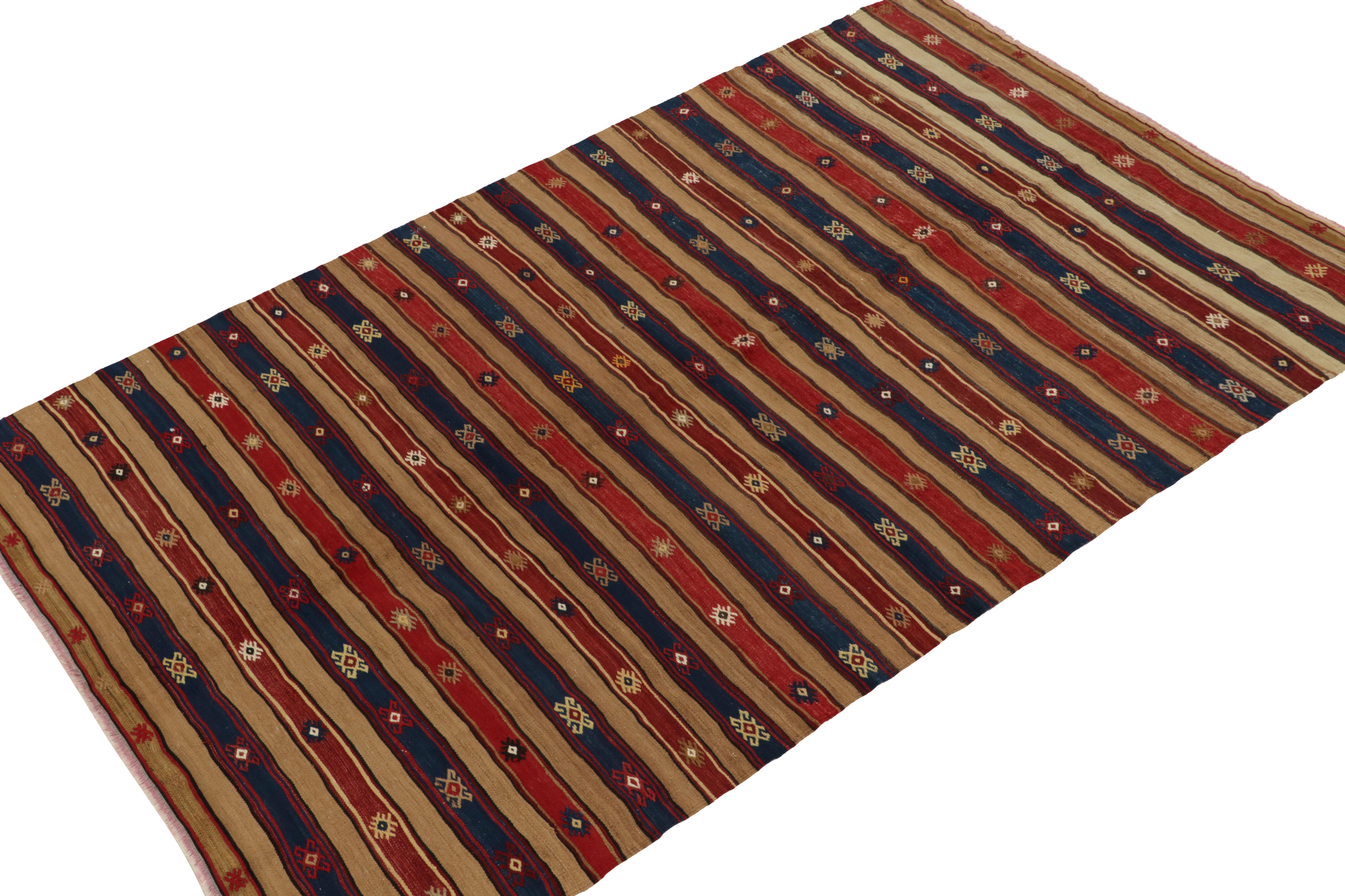 Impeccably hand woven in wool, this vintage kilim rug originates from Turkey circa 1950-1960. The 5x9 Fethiye tribal piece witnesses an outstanding marriage of traditional patterns with stripes in red, blue & beige-brown. Bright motifs lend a more