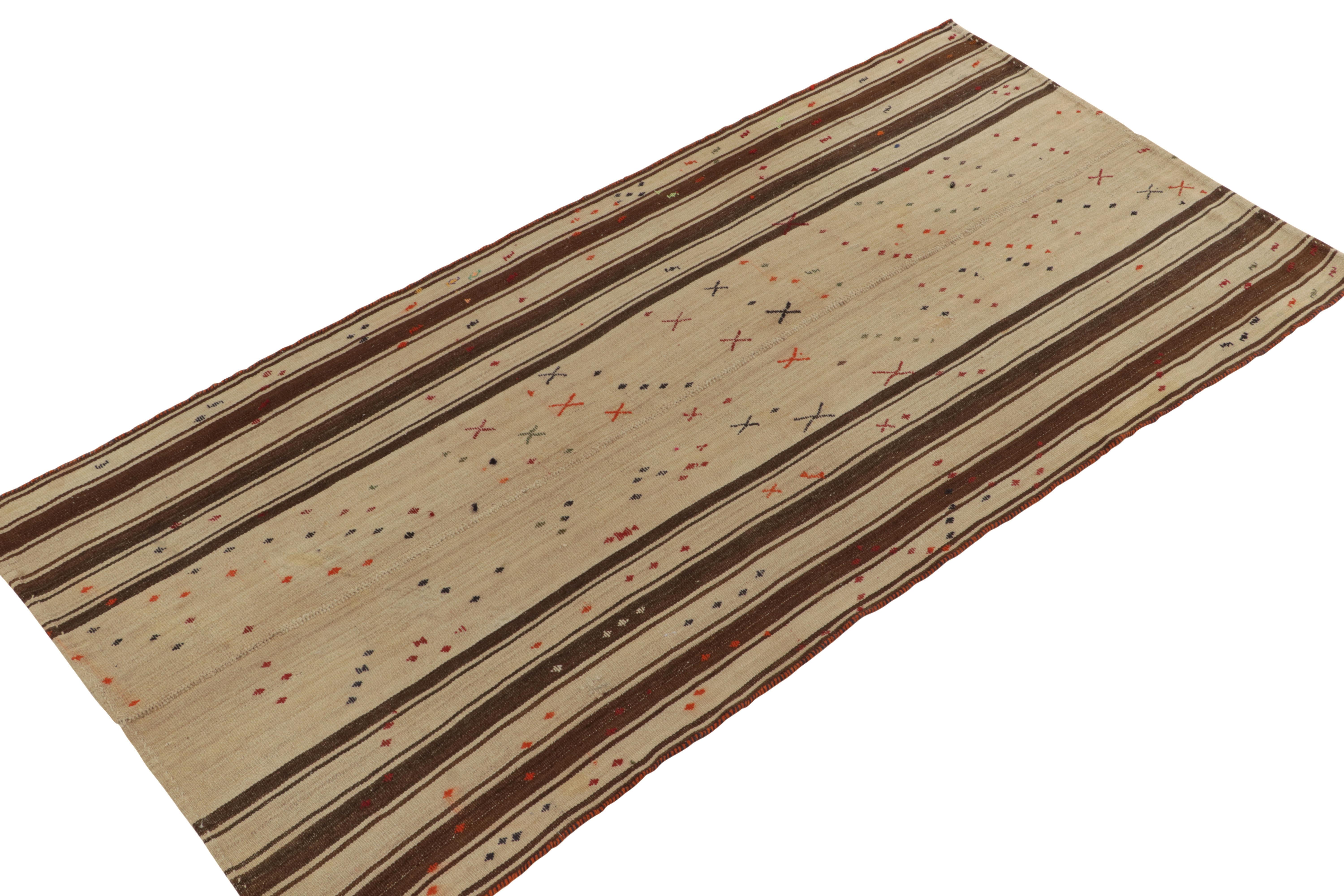 Originating from Turkey circa 1950-1960, a 2x10 mid-century kilim rug now entering our antique & vintage flat weaves curations. Between beige-brown stripes in vertical borders, the rug field enjoys colorful geometric patterns for a
