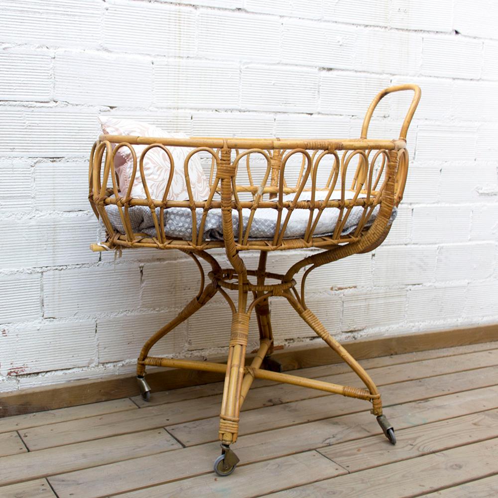 This midcentury vintage cradle is made with a bamboo structure. The oval basin has looping details around the sides and sits on four legs fit with wheels. There is a handle on one side for easy movability.