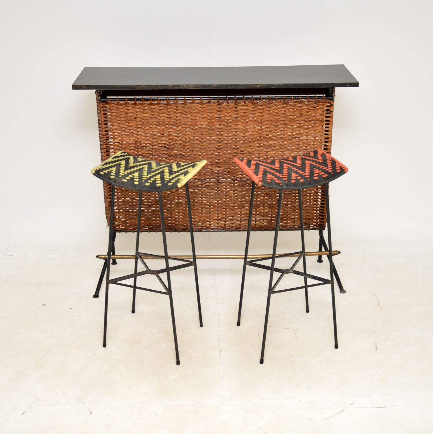 A very stylish and unusual vintage bar with two matching bar stools. This was made in England in the 1950-60’s.

It is extremely well made, the bar has a steel frame with woven rattan around the front and sides. The top is black formica, and there