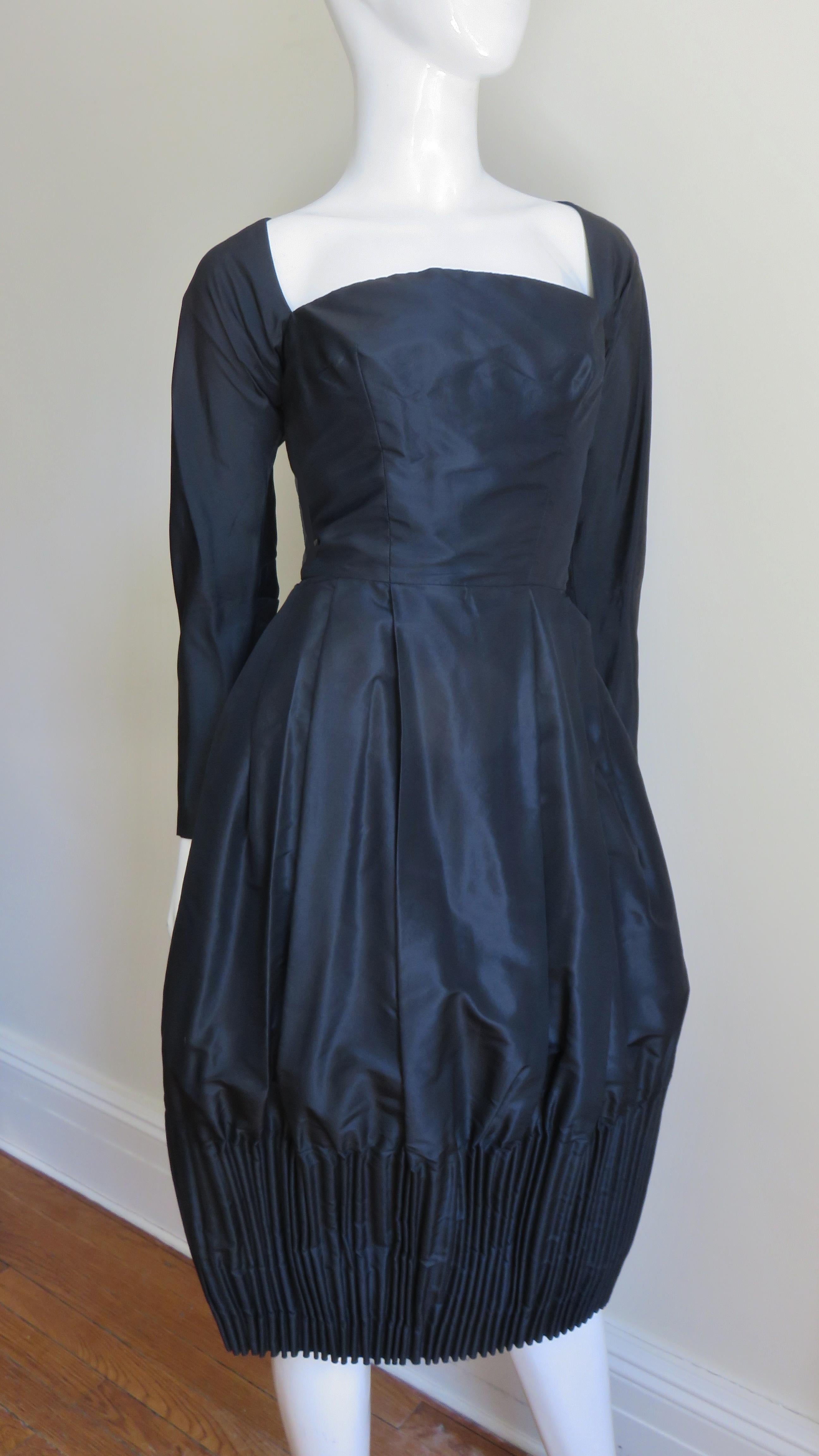A stunning little black silk dress from Viola with a square neckline and a fitted princess seam bodice. The tulip skirt has incredible cartridge pleating around the hem and the sleeve cuffs and dress back have metal painted zippers.  
Fits size