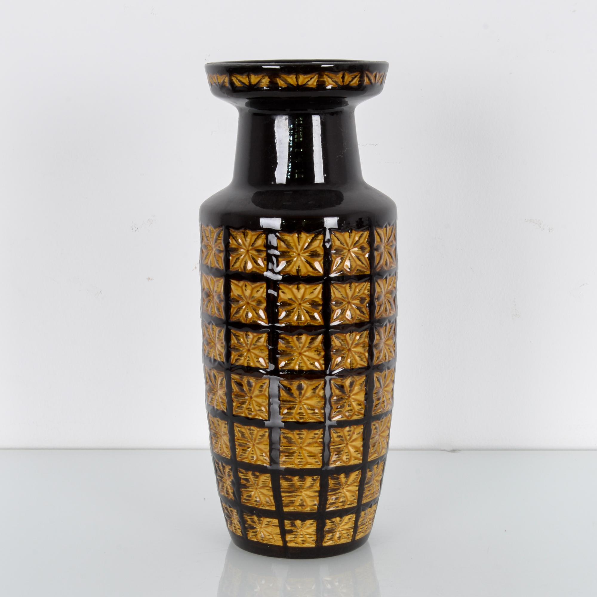 This ceramic vase was made in Germany, circa 1950. Diamond-shaped petals carved in squares form a distinctive geometric pattern on its body. The vase displays a rich, deep brown glaze, which complements the earthy yellow tones of the geometric