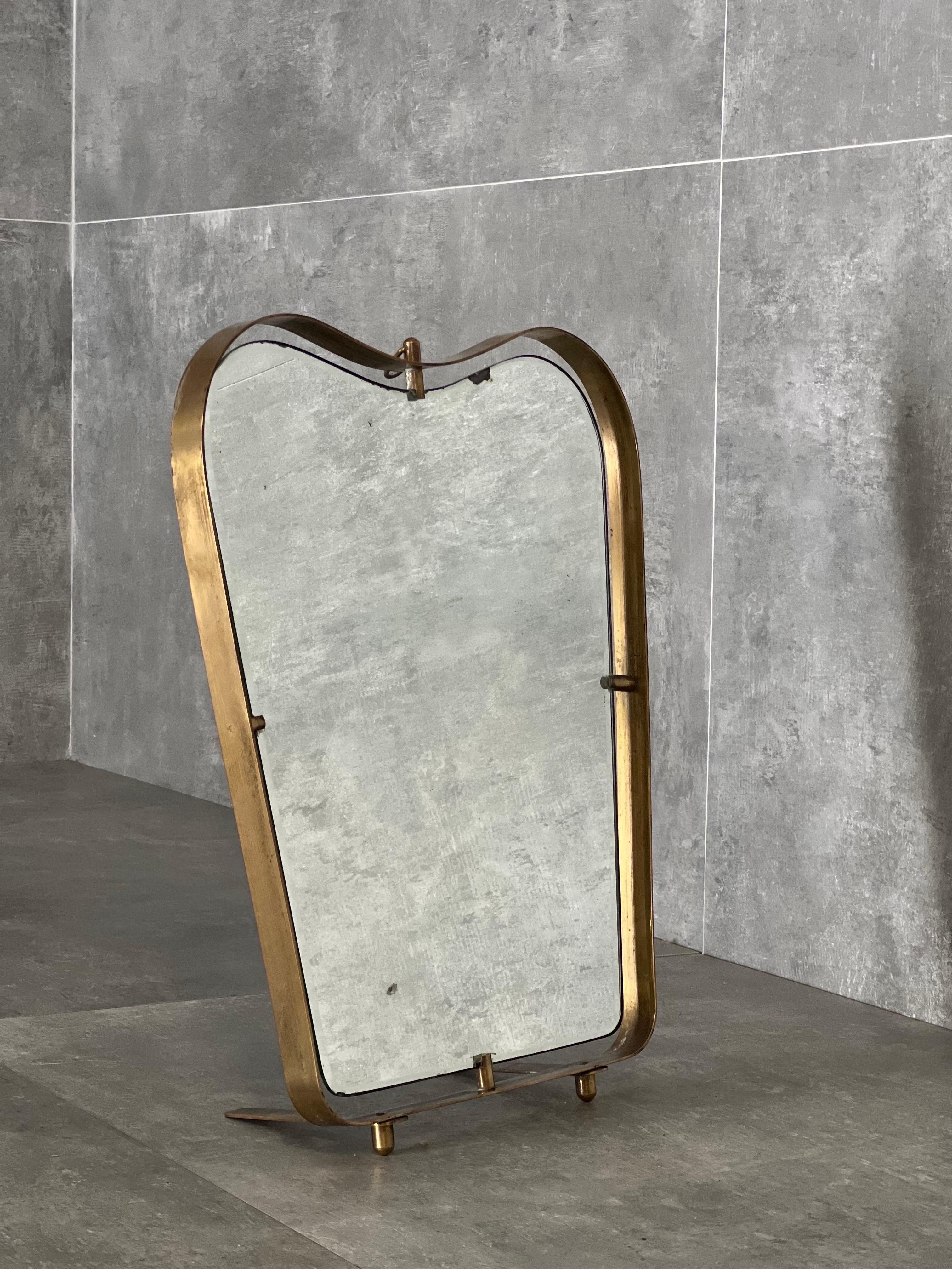 1950s mirror with brass frame attire. to Fontana Arte. This mirror can be used both for wall hanging or as a table mirror thanks to adjustable brass legs on the base and a hanging brass ring on the top. 