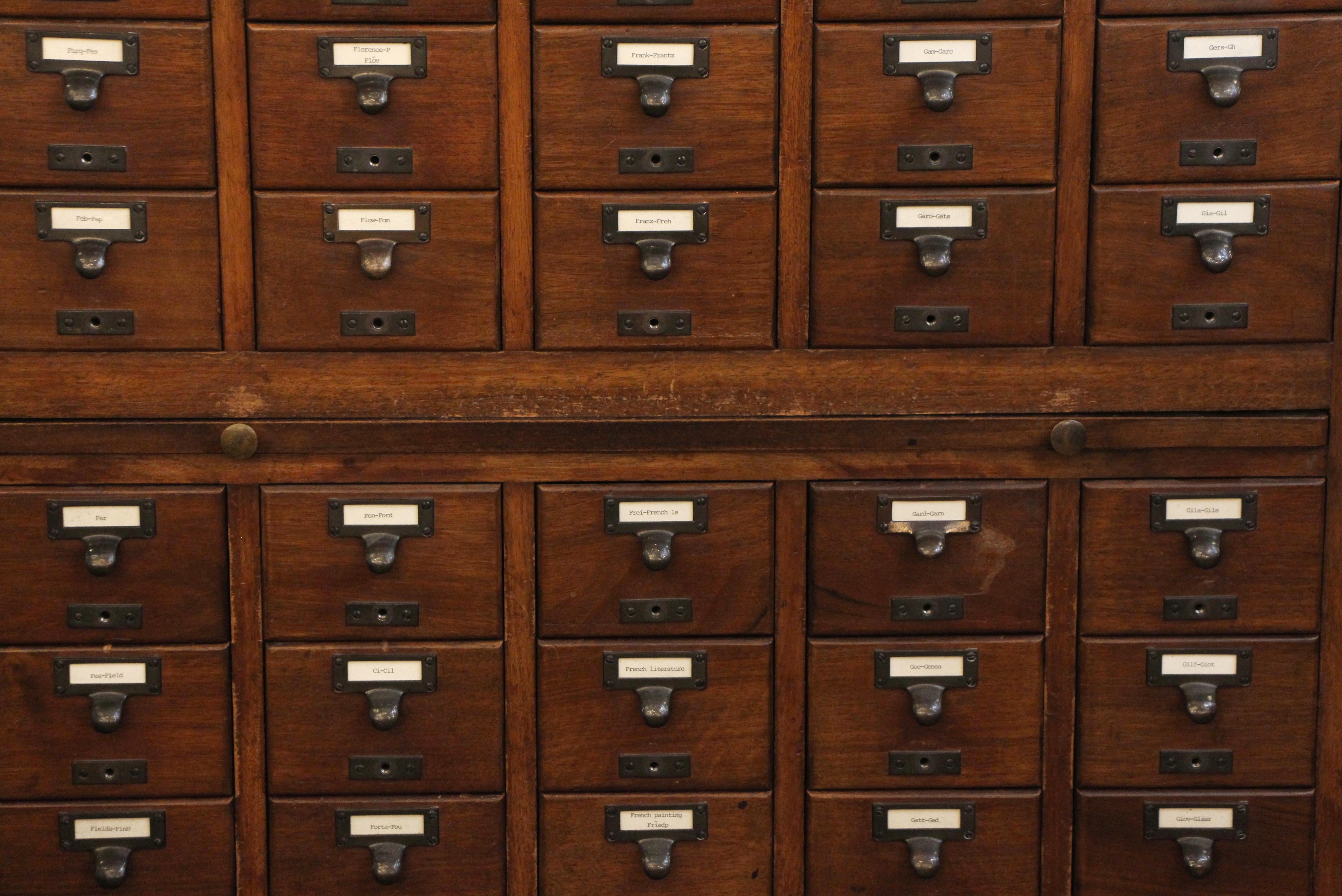 1950s dark wood tone walnut card catalog with 55 drawers and original brass hardware. Two slide out trays. There is no backing to this piece. Original construction. Please see all photos. This can be seen at our 2420 Broadway location on the upper