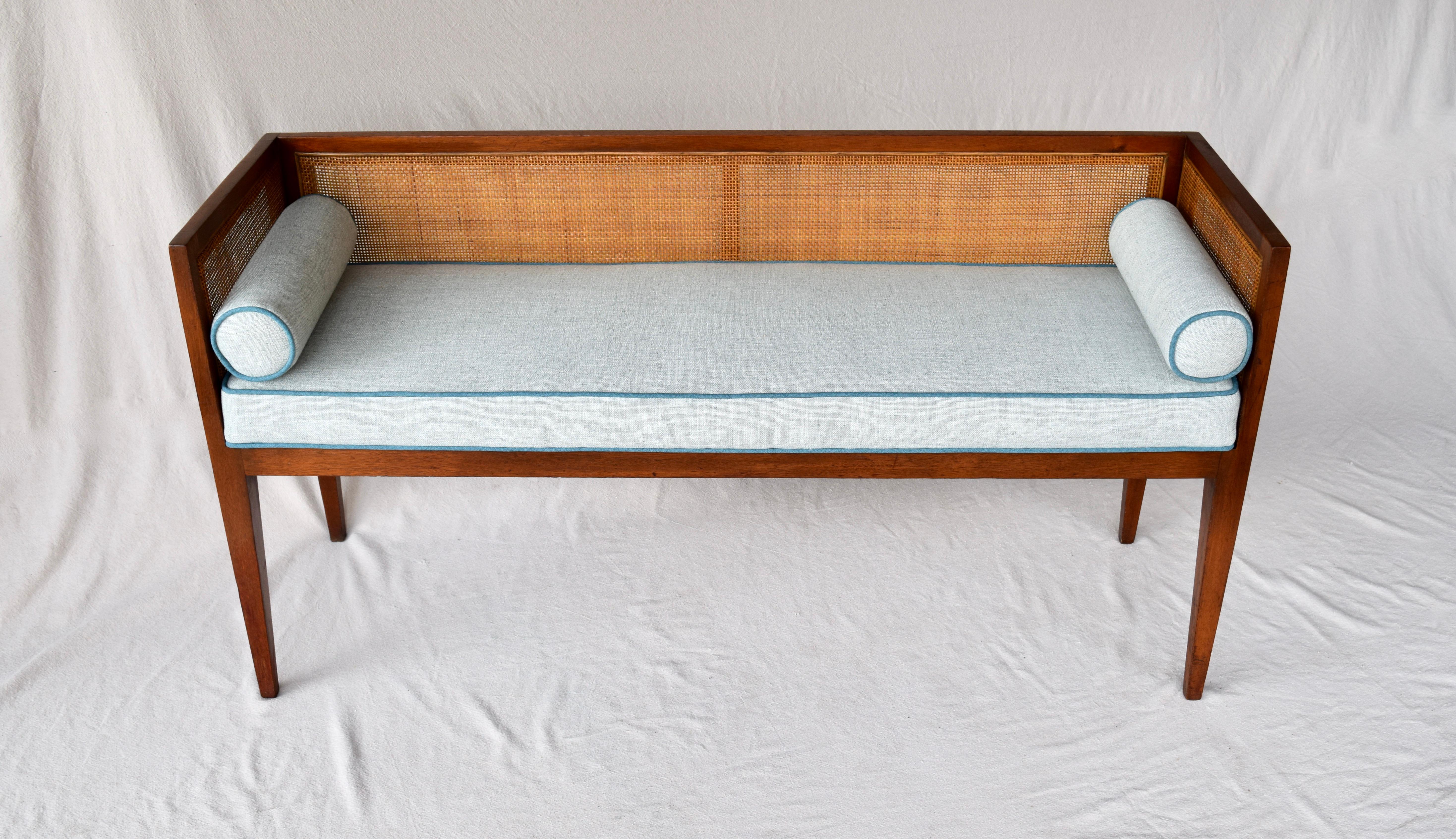 Solid walnut Mid-Century Modern window bench or settee attributed to Edward Wormley for Dunbar. Lithe line design constructed of walnut frame with original fine scale caning. Restored seat and bolster cushions are upholstered is soft blue linen
