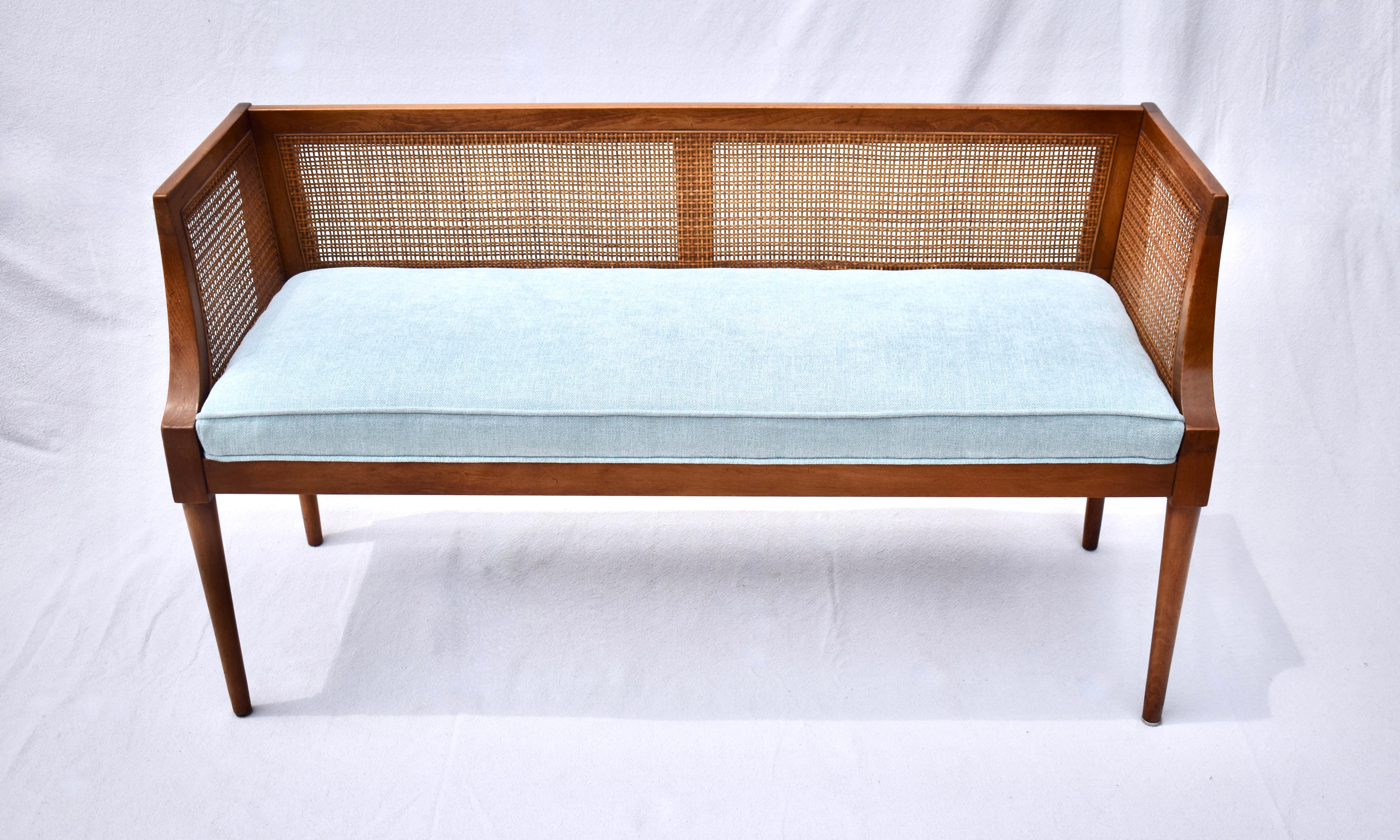 A solid walnut Mid-Century Modern window bench or settee attributed to Edward Wormley for Dunbar. Lithe lines with swag arm design features original fine scale caning & new seat cushion upholstered in soft blue cotton Chenille.