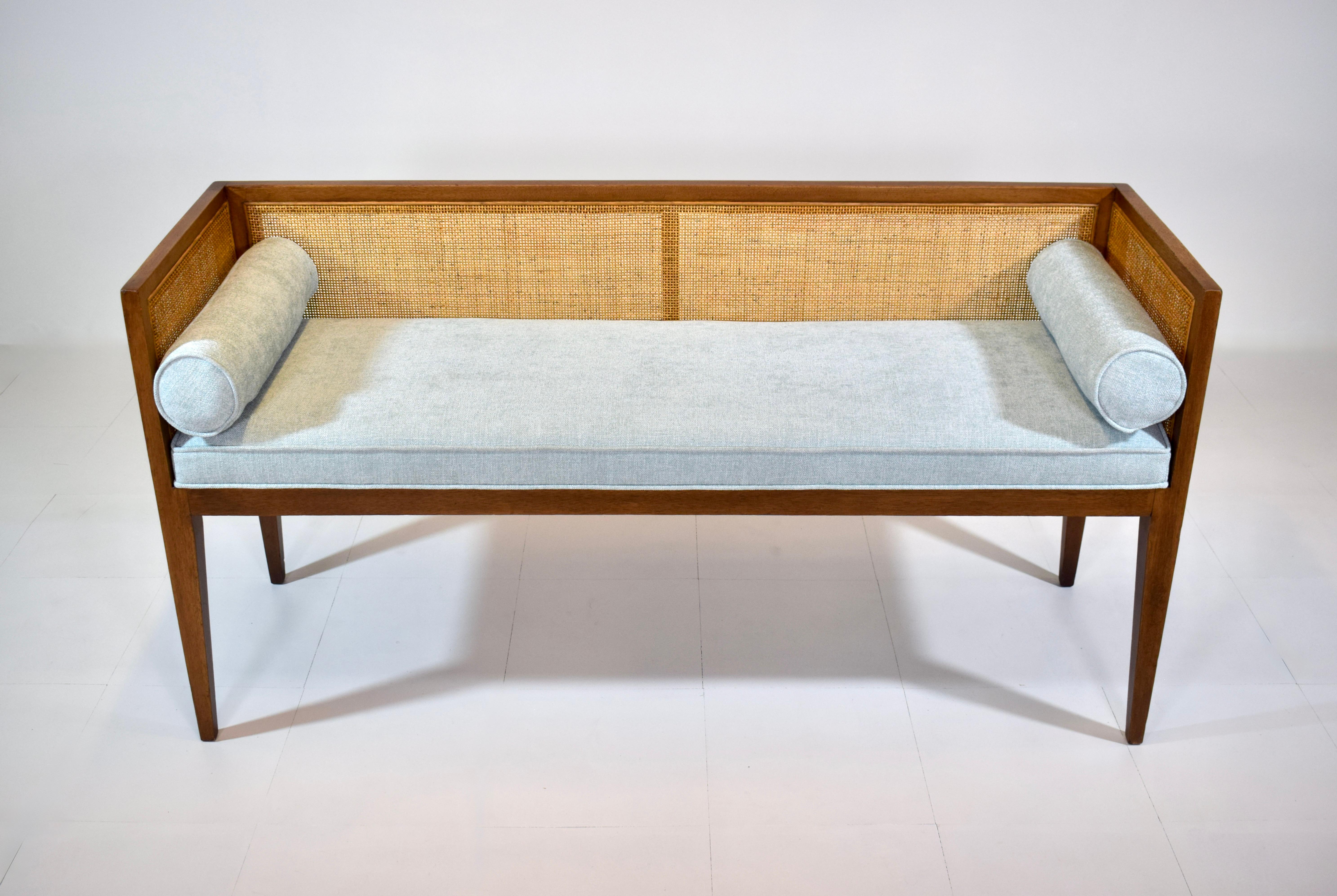 A solid walnut Mid-Century Modern window bench or settee attributed to Edward Wormley for Dunbar. Lithe line design constructed of fully restored walnut frame with new fine scale caning, seat and bolster cushions upholstered in soft blue cotton