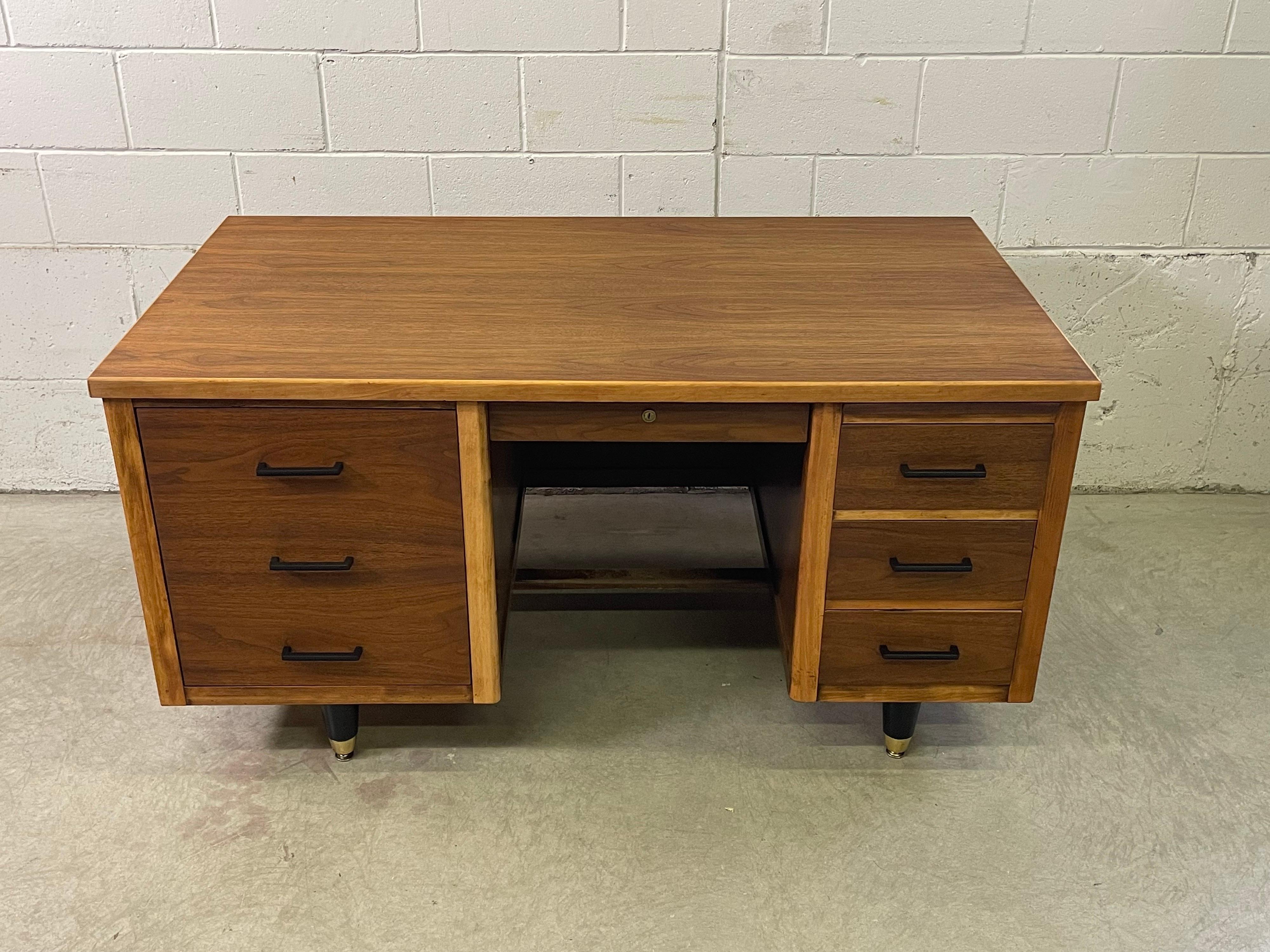Vintage 1950s walnut wood tanker desk by Imperial Furniture. The desk has three drawers on one side and deep open storage on the other. There is also a small drawer in the middle. The desk also has a pull out for writing. The pulls and the legs are