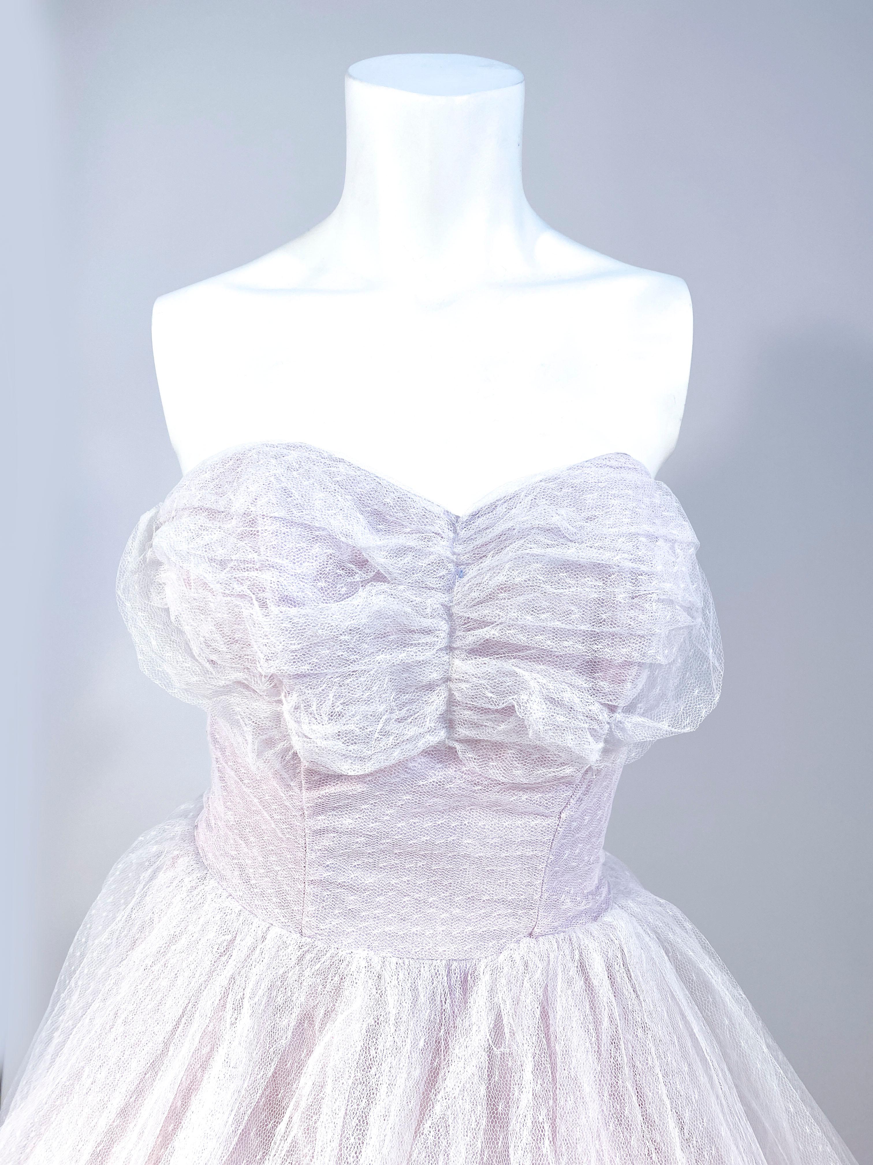 1950s white tulle dress with a lavender colored satin lining. The Bodice of the dress has ruching decorating the bust. The skirt is entirely made of a white tulle gathered at the waist extending to Austrian poof draping finished with six layers of