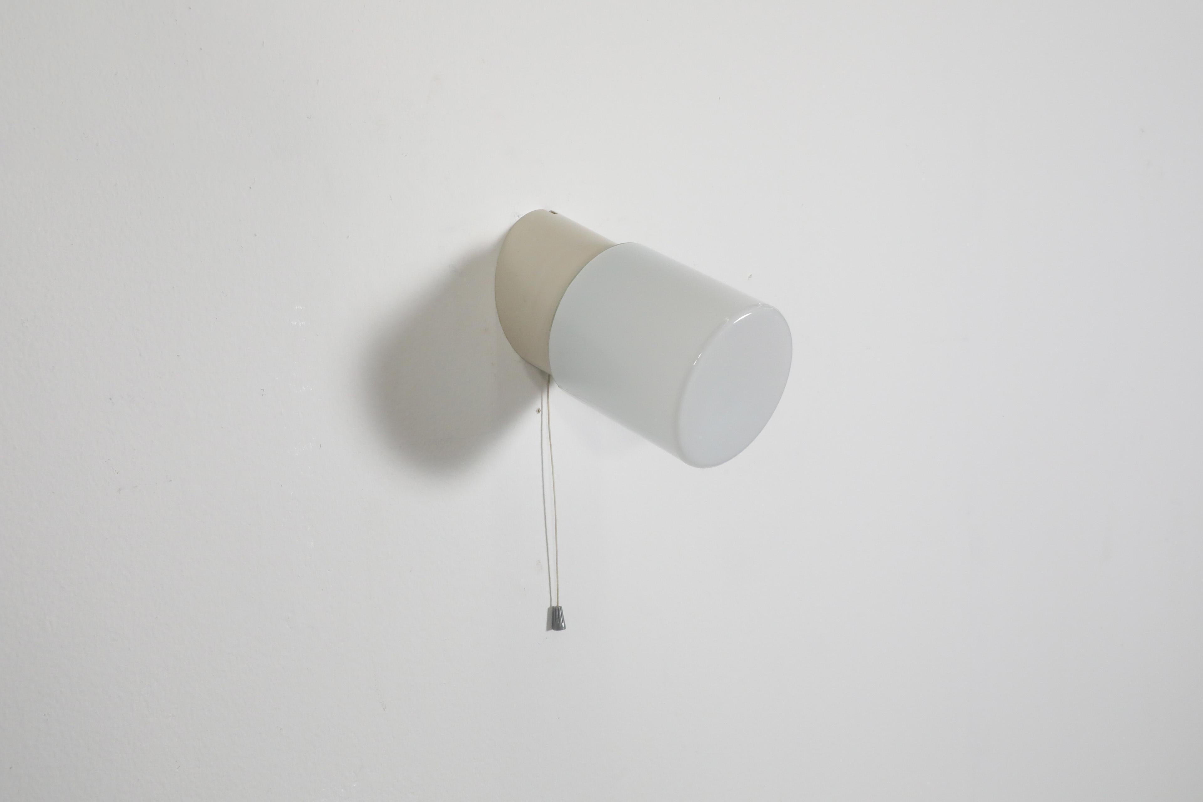 White cylindrical wall or ceiling sconce with angled bakelite base, white cylinder glass shade and pull string switch. This lamp is for hard wire installation, but a cord can be added, as there are notches in the base. In original condition with