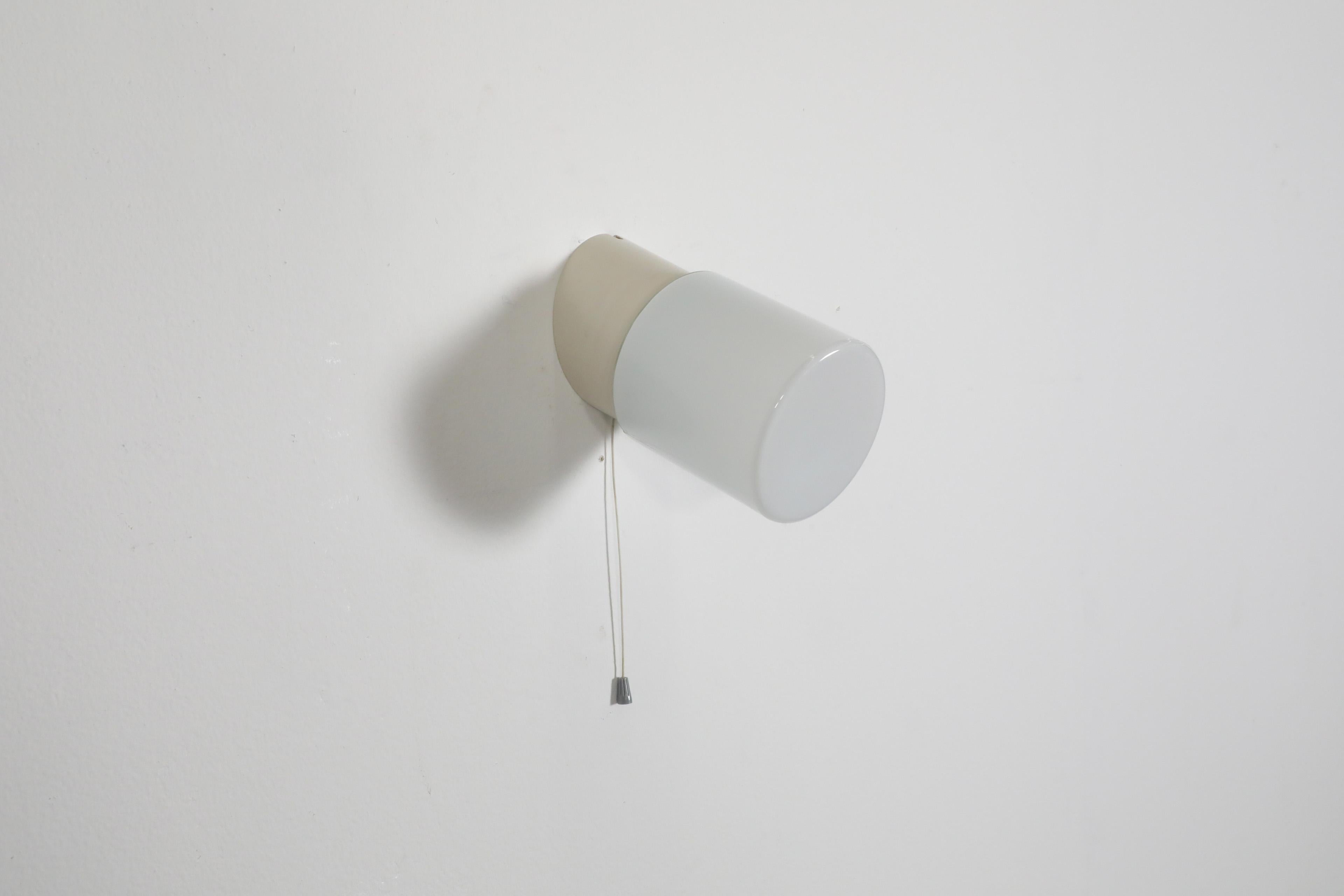 Applique cilindrica bianca da parete o soffitto con base angolare in bachelite, paralume in vetro cilindrico bianco e interruttore a tirante. Questa lampada è destinata all'installazione a filo, ma è possibile aggiungere un cavo, in quanto sono