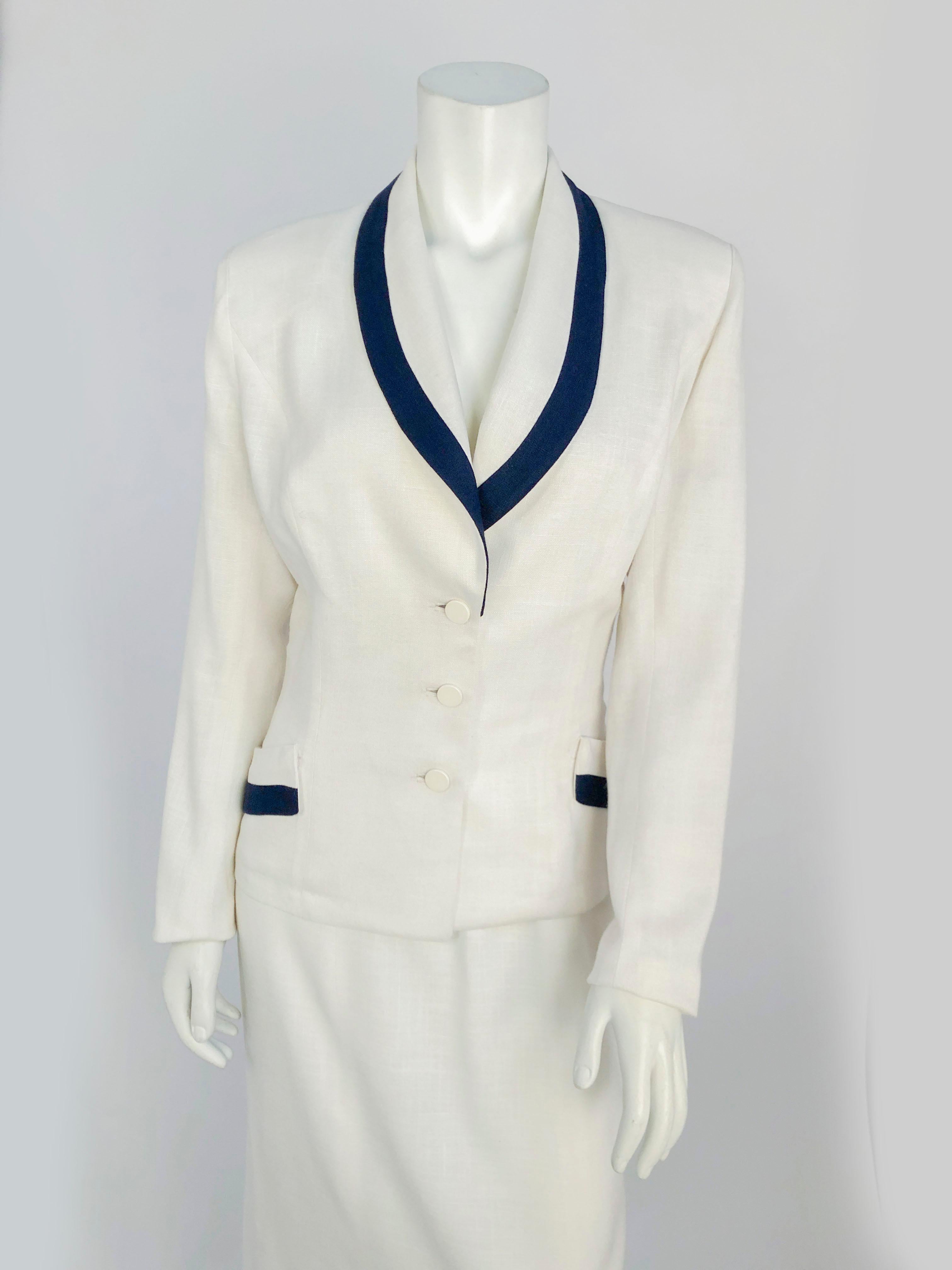 1950s White linen suit with navy boarder along the shawl collar and pockets. The jacket with fitted with inset buttons and two functional pockets. The skirt has a straight silhouette and an applied waist band.