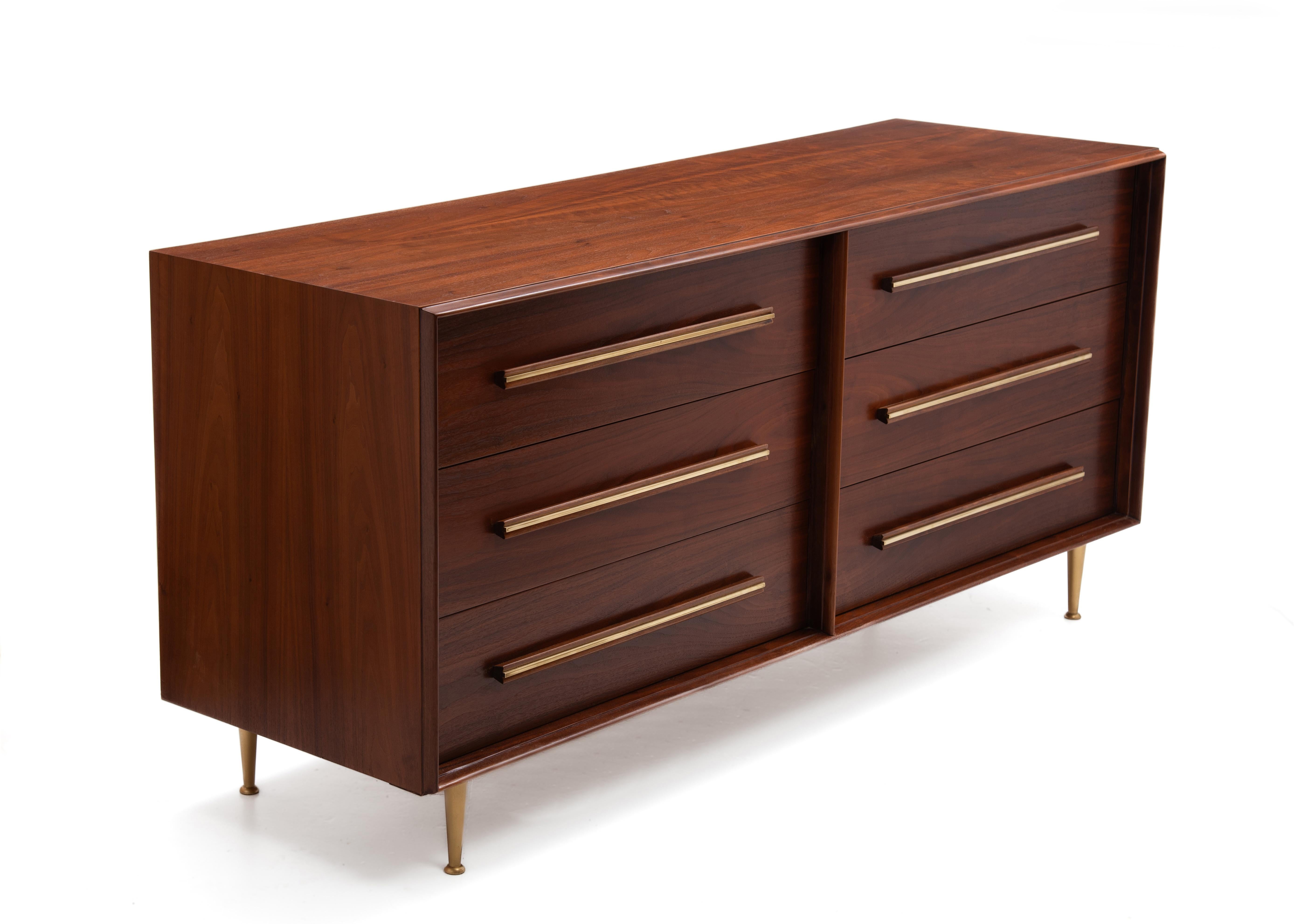Un imponente comò a sei cassetti degli anni '50 realizzato dalla Widdicomb Furniture Company e disegnato da T.H. Robsjohn-Gibbings. Cassetti perfettamente intonati, maniglie in noce massiccio, intarsi in ottone e piedini in ottone. Abbiamo anche una