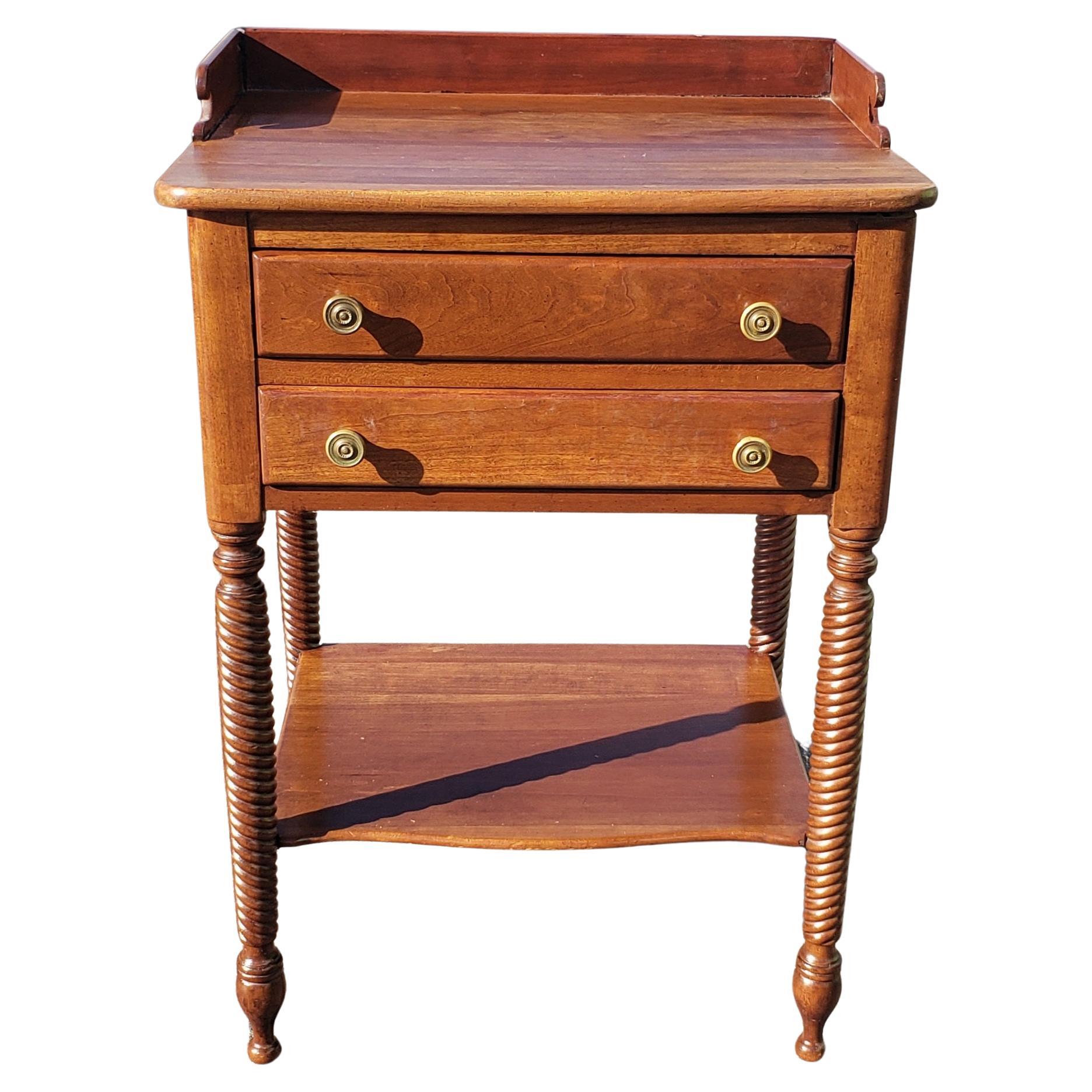 A vintage side table from the Willett Furniture Company in solid Kentucky cherry. The table has rope turned legs, round brass pulls, two drawers and a gallery. Beneath there is a shaped shelf between the four legs. Willett produced extremely popular