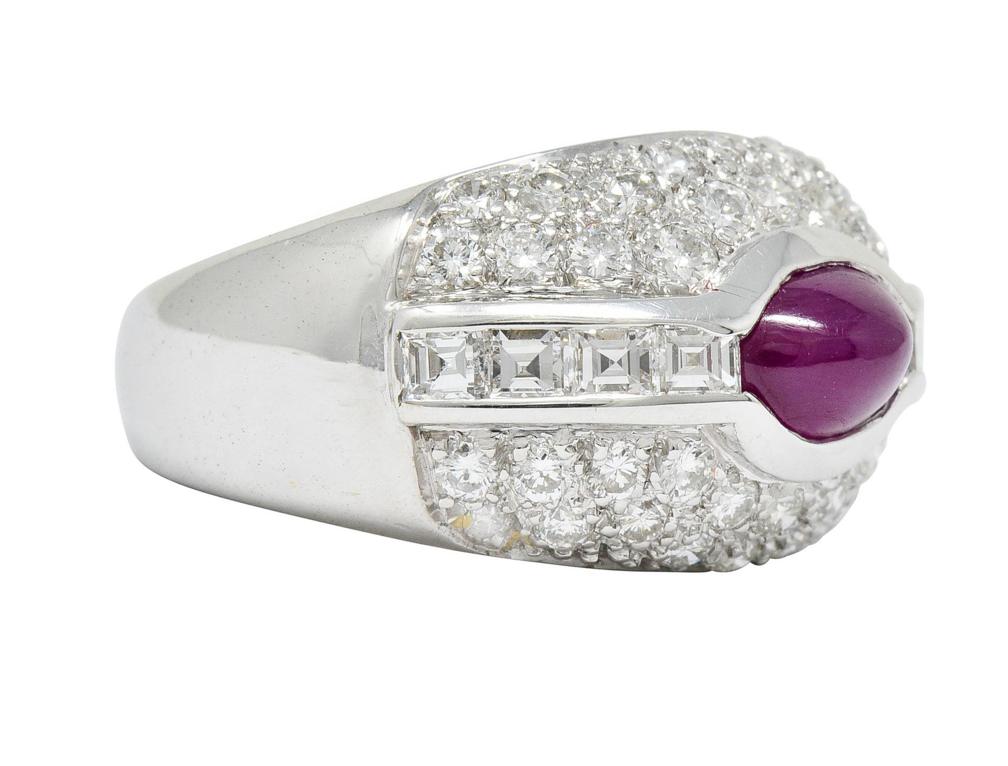 Bombay style band centers on oval ruby cabochon weighing approximately 1.00 carat

Purplish-red in color and translucent with natural inclusions

Half bezel set in an eyelet motif and flanked by channel set square step cut diamonds

Weighing