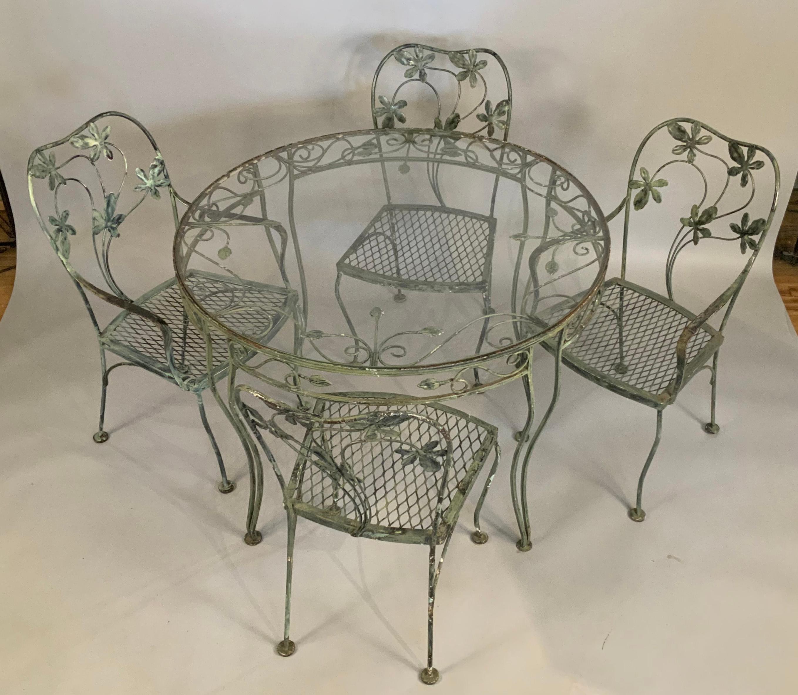 A beautiful vintage 1950's wrought iron dining set by Woodard. Wonderful large scale floral in the curved backs of the chairs, and a large glass top round table. all in good original condition, with some surface rust around the edge of the table as