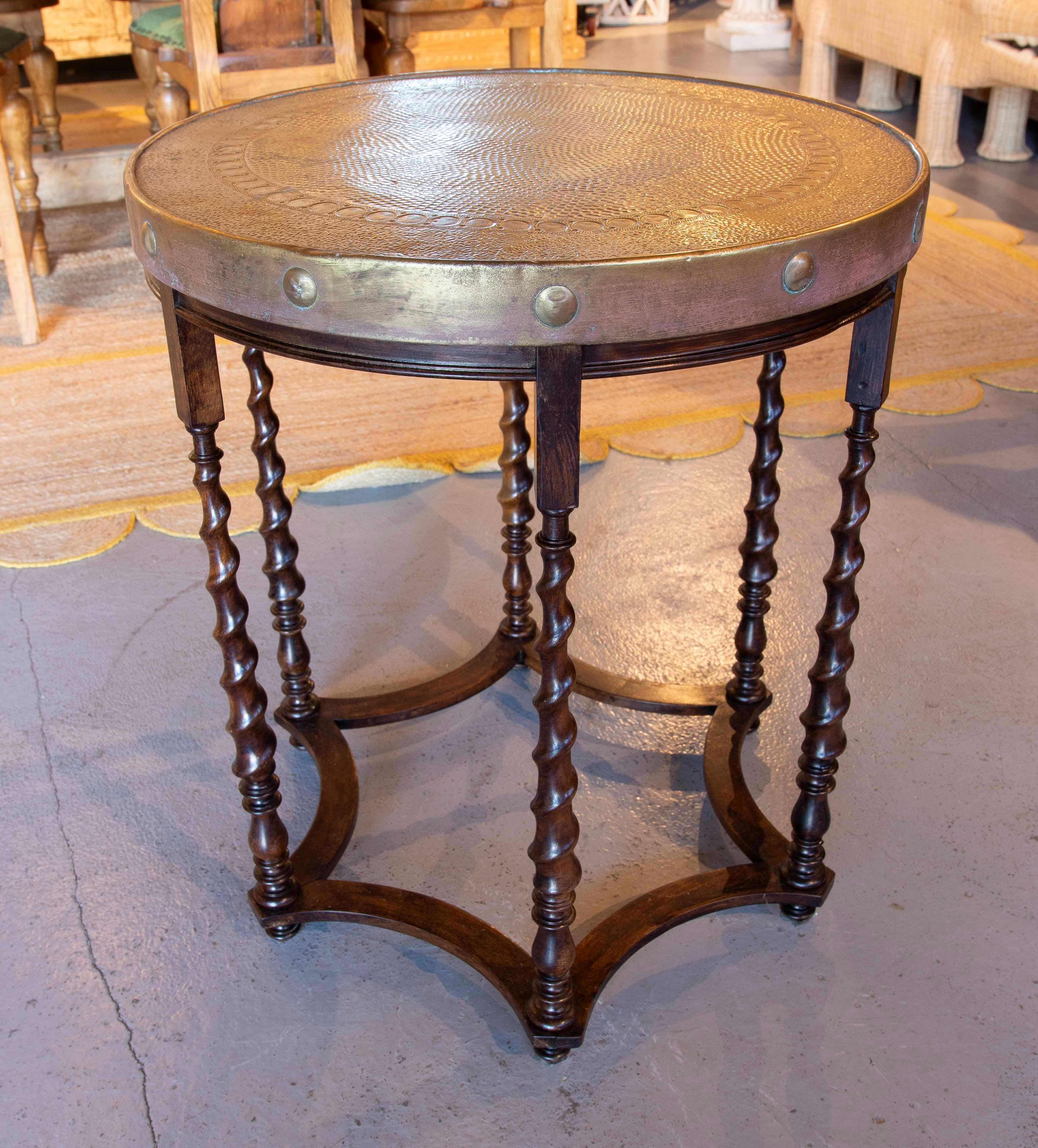 Exquise table d'appoint avec une base en bois tourné et un remarquable plateau circulaire en laiton gaufré, décoré de rivets sur le bord. Son design allie la chaleur du bois à l'élégance du métal, créant ainsi une pièce sophistiquée et unique.