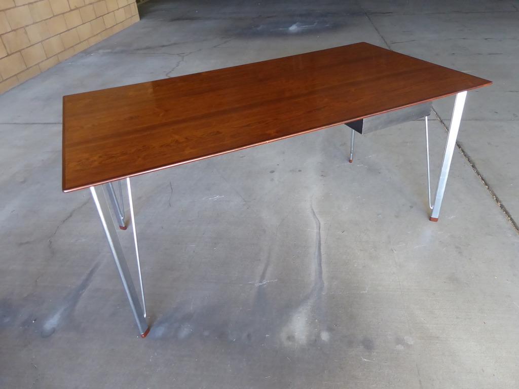 A 1950s rosewood topped desk or writing table with one drawer by the renowned Scandinavian designer Arne Jacobsen. Manufactured by Fritz Hansen. The base has metal legs that terminate with elegant little rosewood feet.