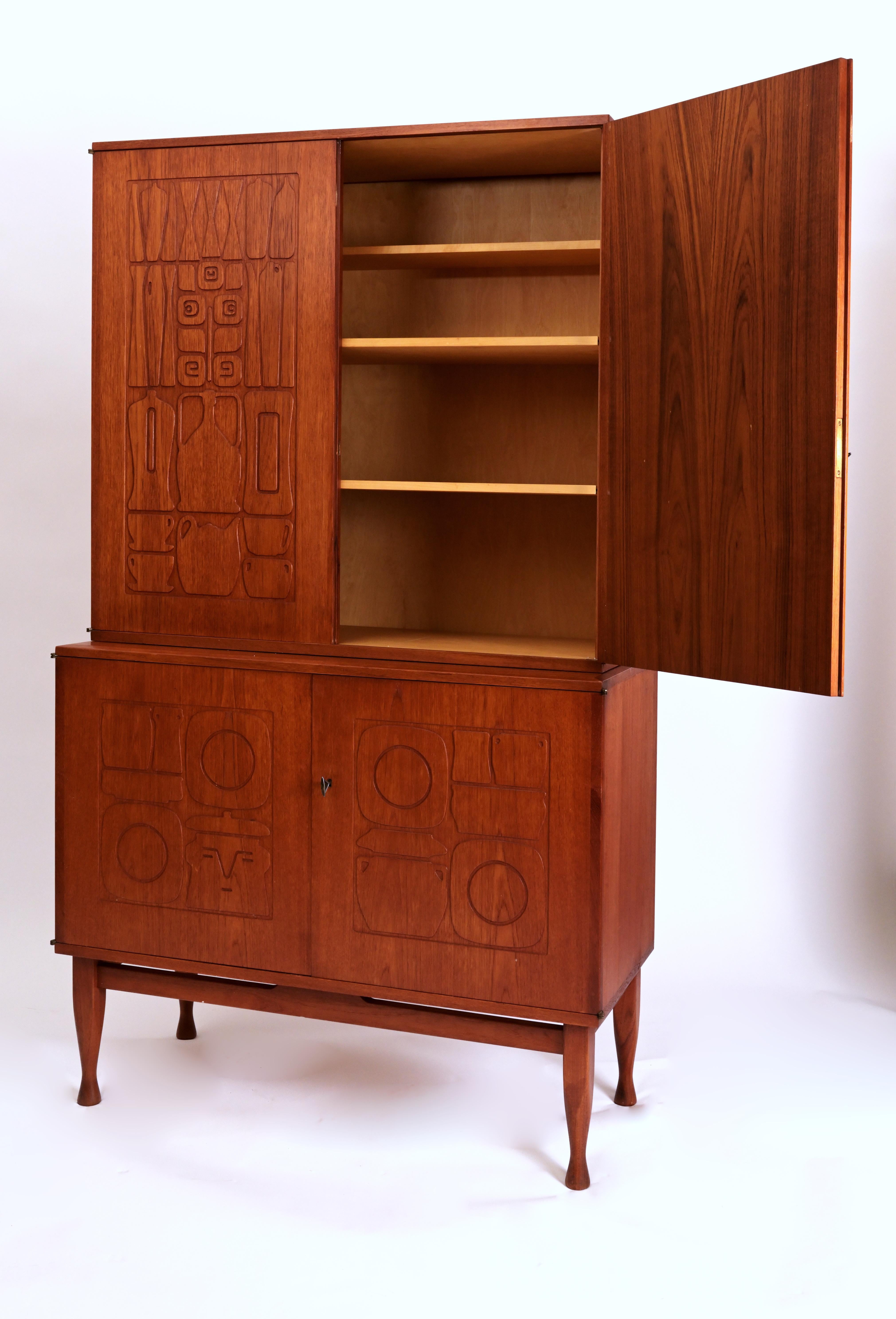A 2 part teak cabinet by Swedish designer Yngve Ekstrom (1913-1988) for Westbergs Furniture. The two park teak cabinet features doors with hand carved decorations of jars, bottles and other playful designs. The interiors are fitted with adjustable