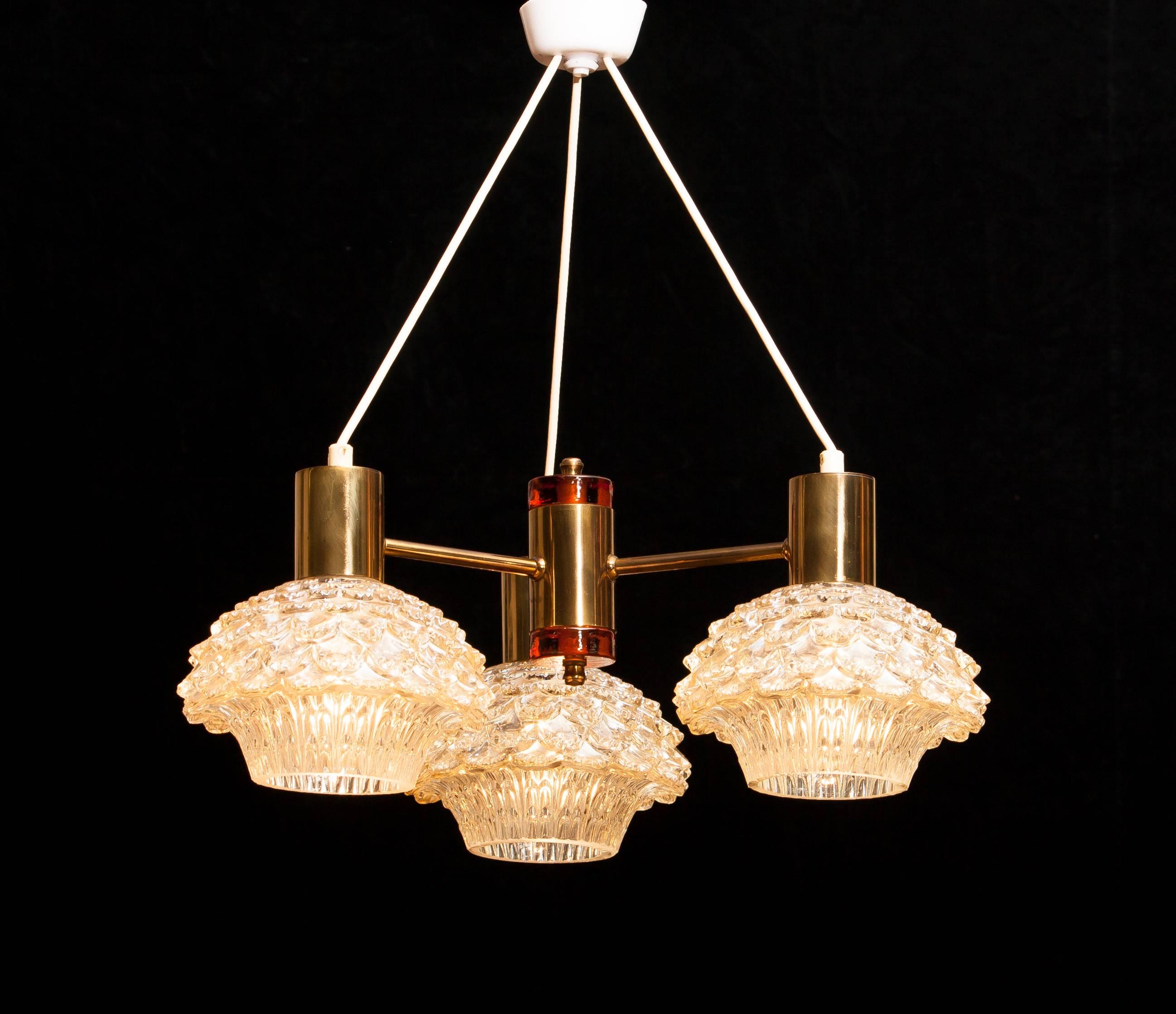 Beautiful chandelier designed by Carl Fagerlund for Orrefors, Sweden.
This lamp has three brass arms with amazing glass shades.
In the middle a brass cillinder with on the top and bottom an amber glass element.
It is in a very nice