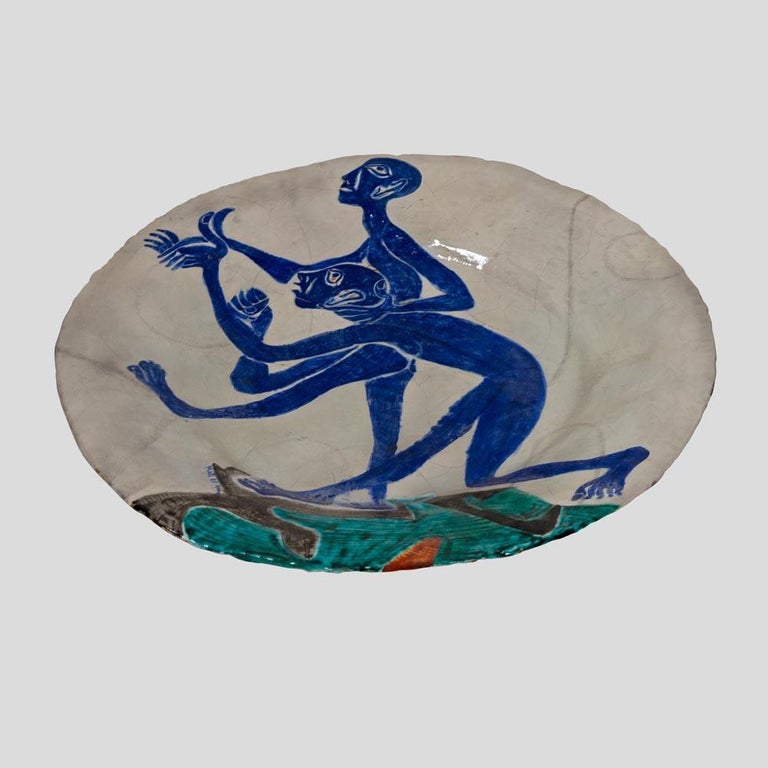 1950s Art glazed Ceramic Charger Painted with two stylised blue figures suggesting dance movement on an off white background with earth brown and grass green soil with a touch of orange. A wall decor created signed and dated 1954 under the glaze by