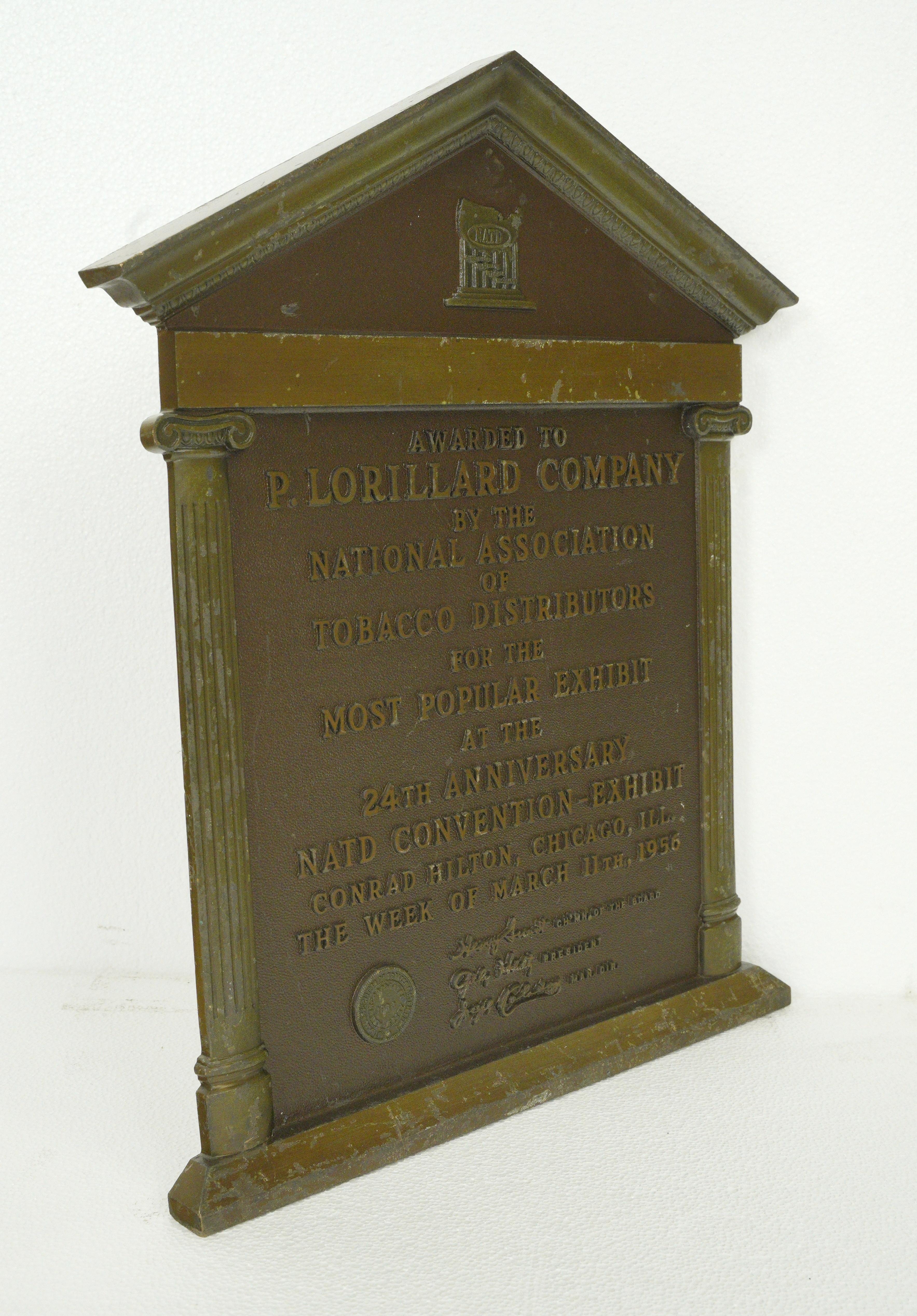 Diese Plakette ist mit der folgenden Inschrift versehen: Award to P. Lorillard Company by the National Association of Tobacco Distributors for the Most Popular Exhibit at the 24th Anniversary NATD Convention - Exhibit, Conrad Hilton, Chicago ILL.