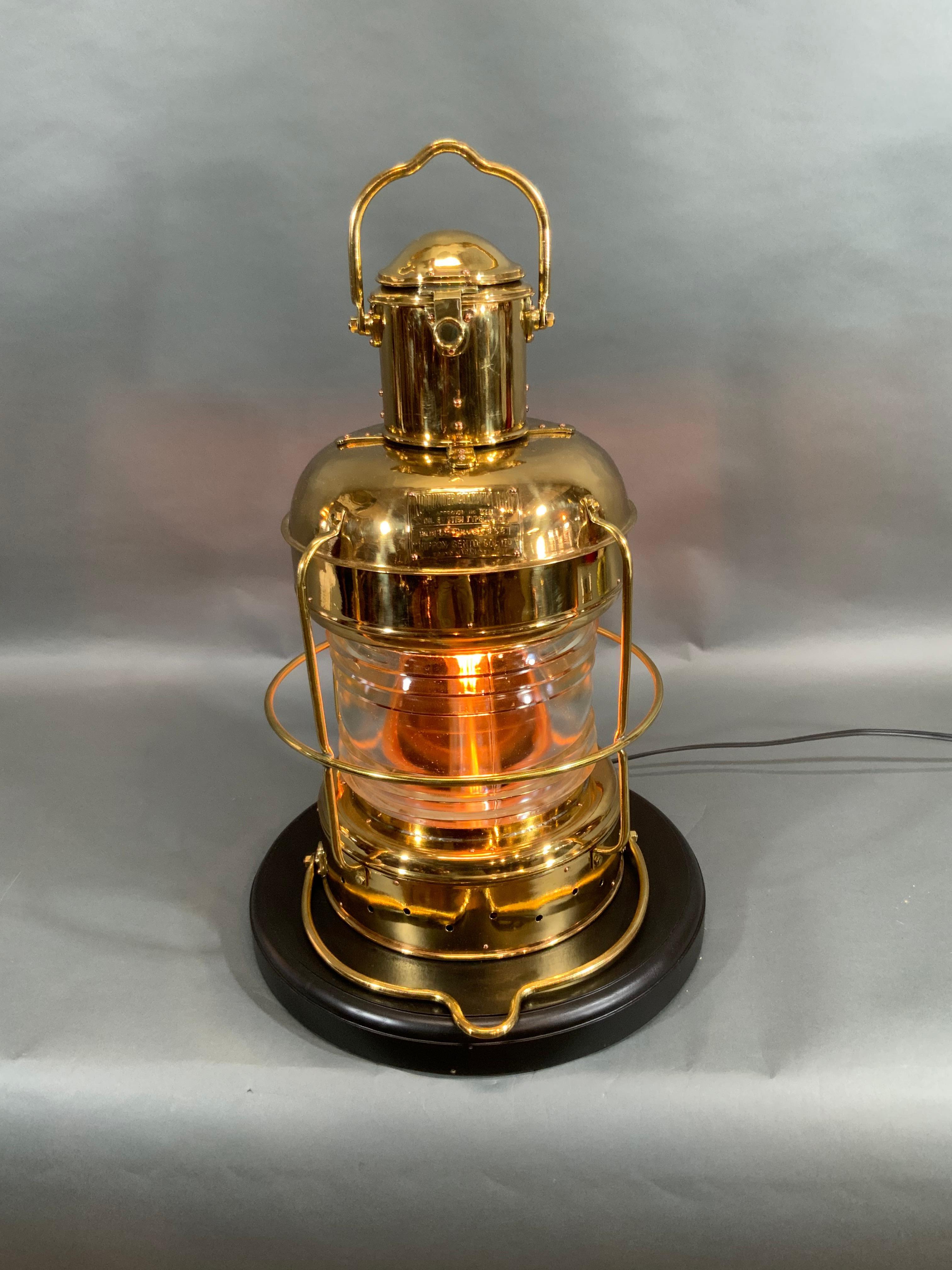 Solid brass ship's anchor lantern with glass Fresnel lens. Wired with electricity. Japanese maker's badge from by Nippon Sento Co. LTD, Tokyo, Japan, dated 1958. Meticulously polished and lacquered. Mounted to a wood base.

Overall dimensions: