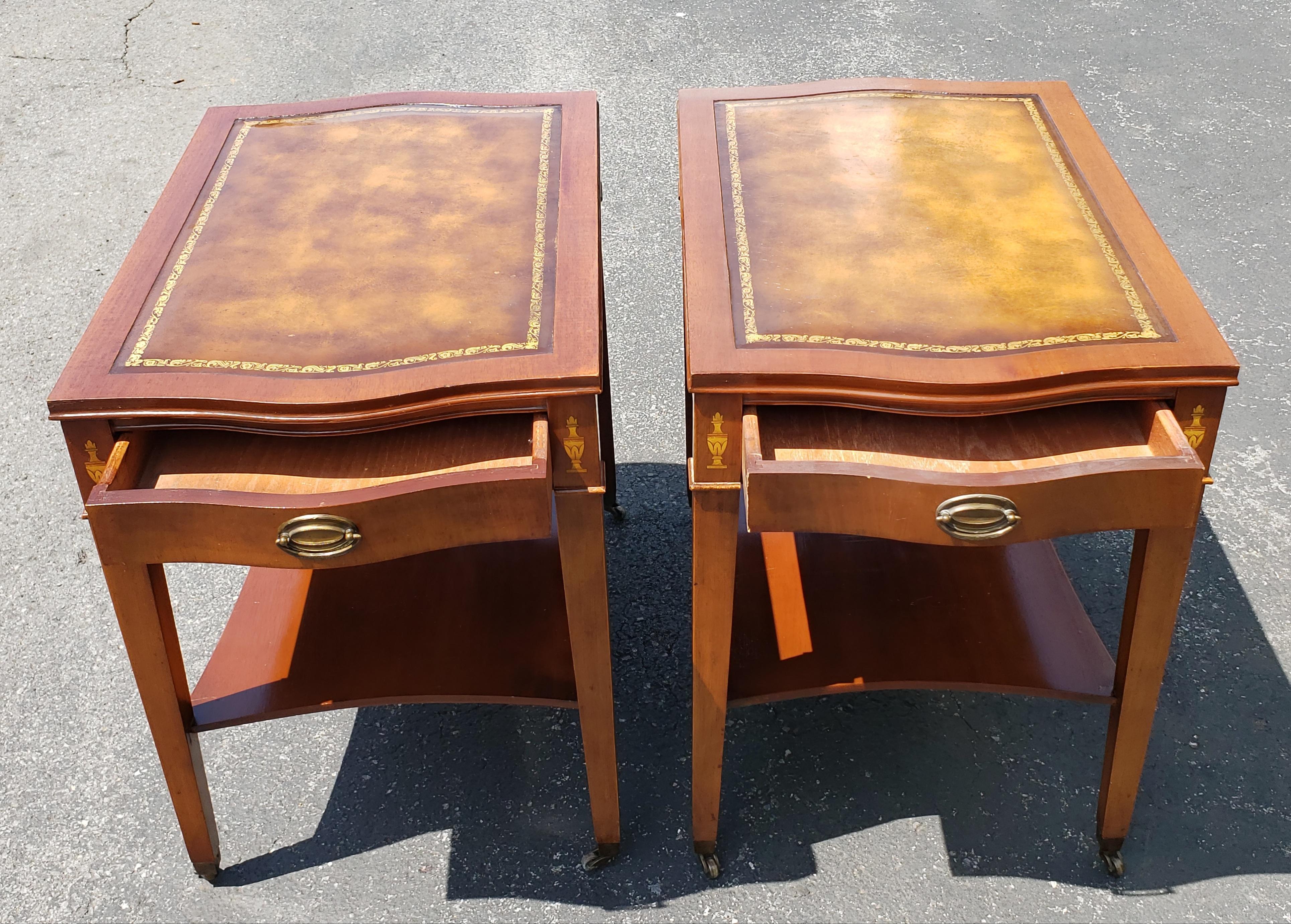 A well kept pair of 1958 Hollywood Regency Mahogany with inlays  and Tooled Leather Top and Gilt Stencil Two tier side Tables on original wheels. Very good vintage condition. Mesure 17.75