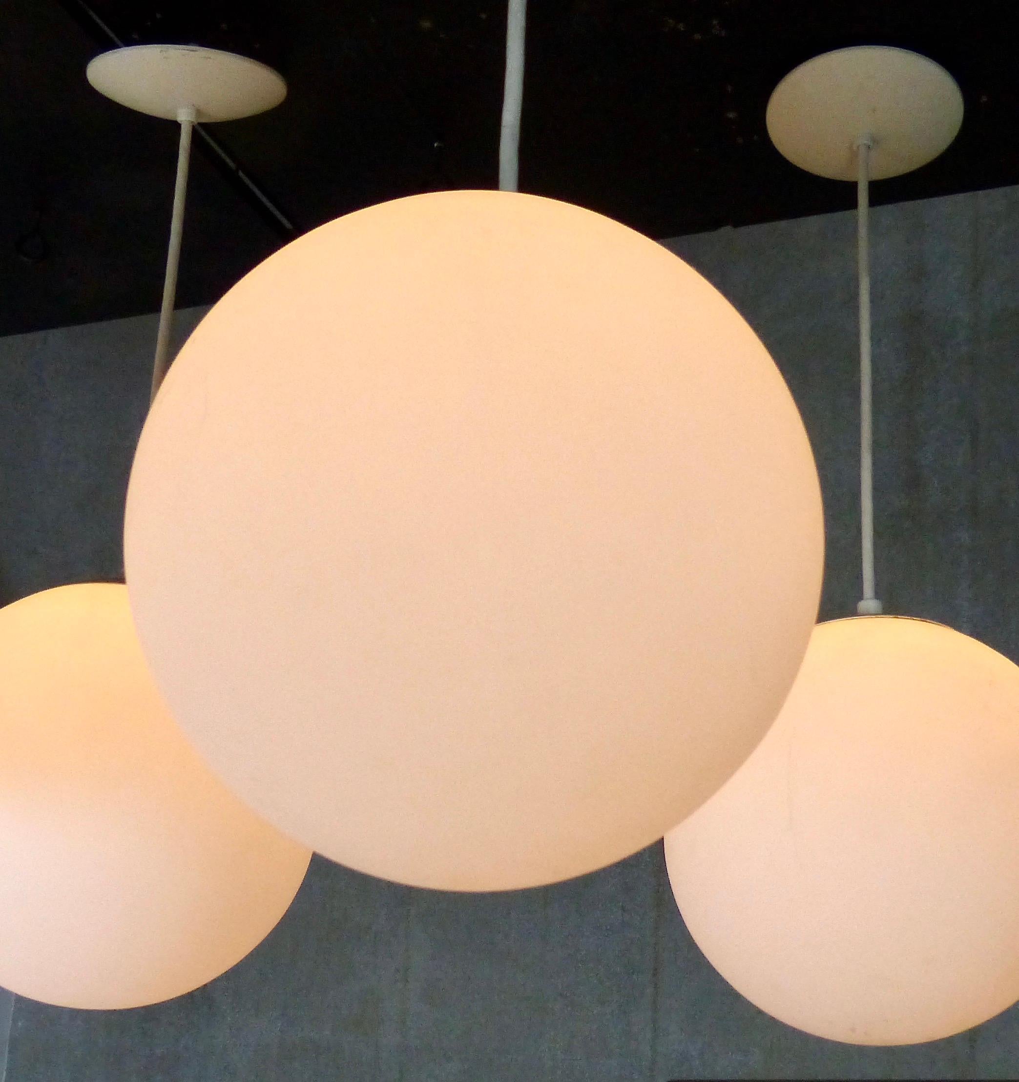 Classic modern milk glass globe pendant lights. Currently hanging at 30” high but could be adjusted to meet your design requirements. Re-wired and inspected/approved to current electrical standards; ceiling mounting plate included. Currently eight