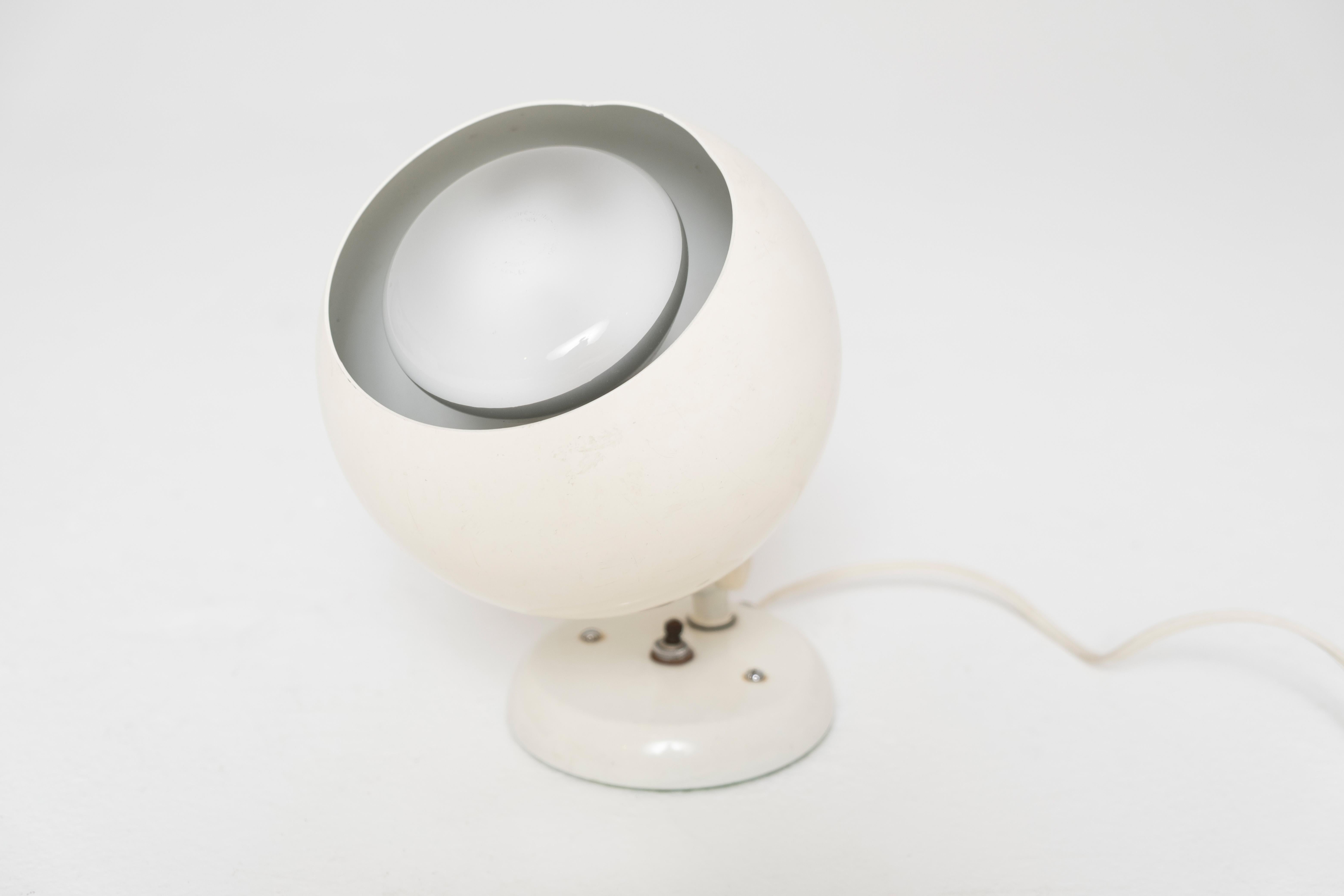 A rare and iconic 1959 table lamp by Remkraft, featuring a spherical white enameled metal shade mounted on a pivoting armature over a rounded weighted base. This classic piece of American mid-century industrial design reflects the burgeoning