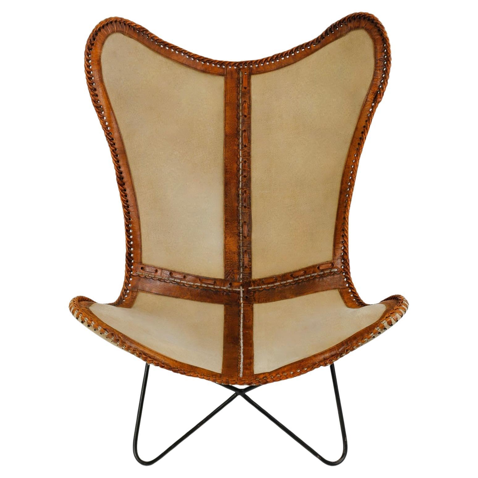Black wrought-iron AA Airborne Butterfly armchair frame from the 1960's, covered with a saddler's cover from the Houlés workshops, made from 4 pieces of cream-colored hide joined by leather strips and edged with a brown patina leather border. 
Chic