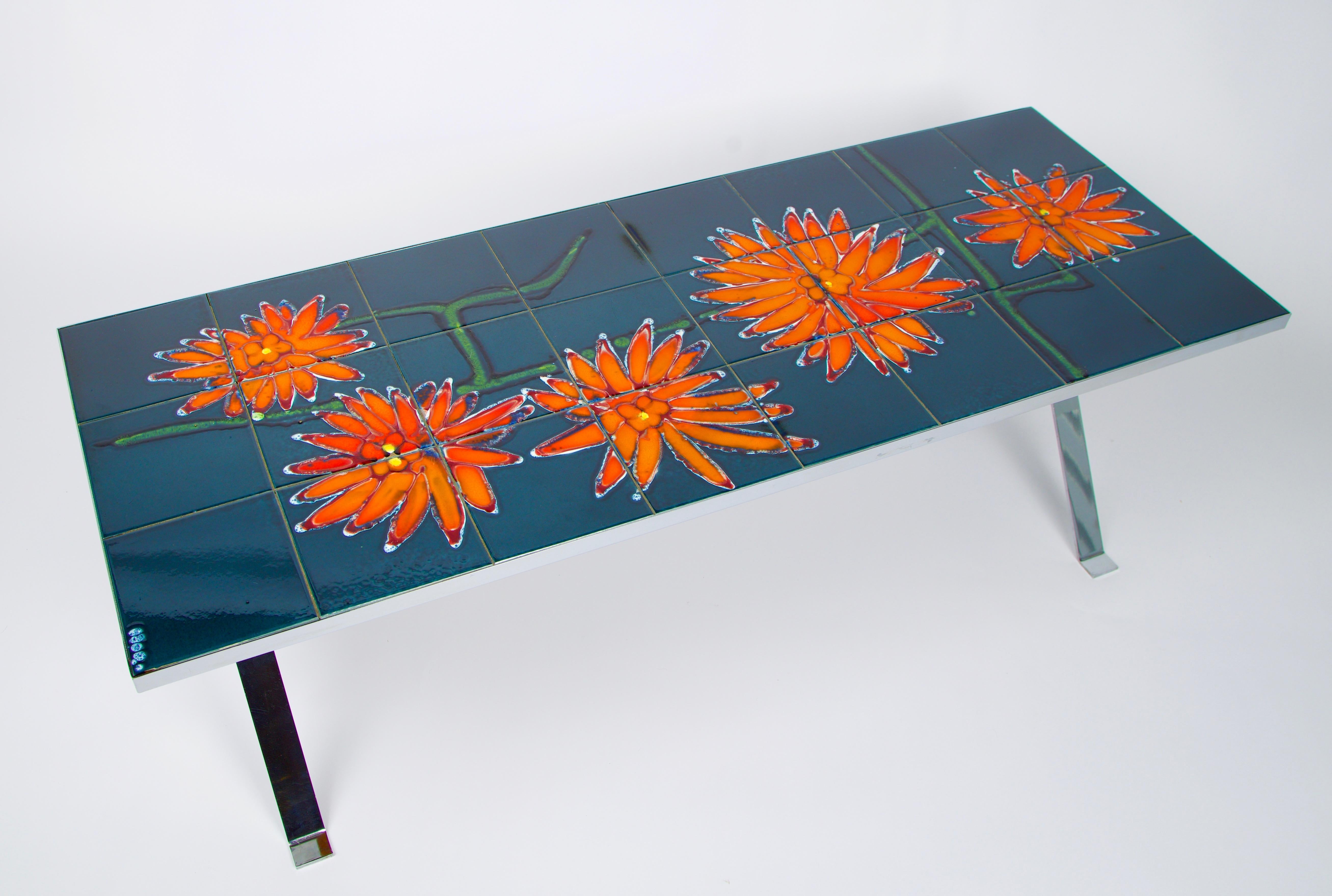 This tile top table is made from hand painted blue ceramic tile with a bright orange abstract floral motif. The tiles rest on a chrome plated base which is supported by a teak stretcher.  It was manufactured and signed by Adri Belgique,  a design