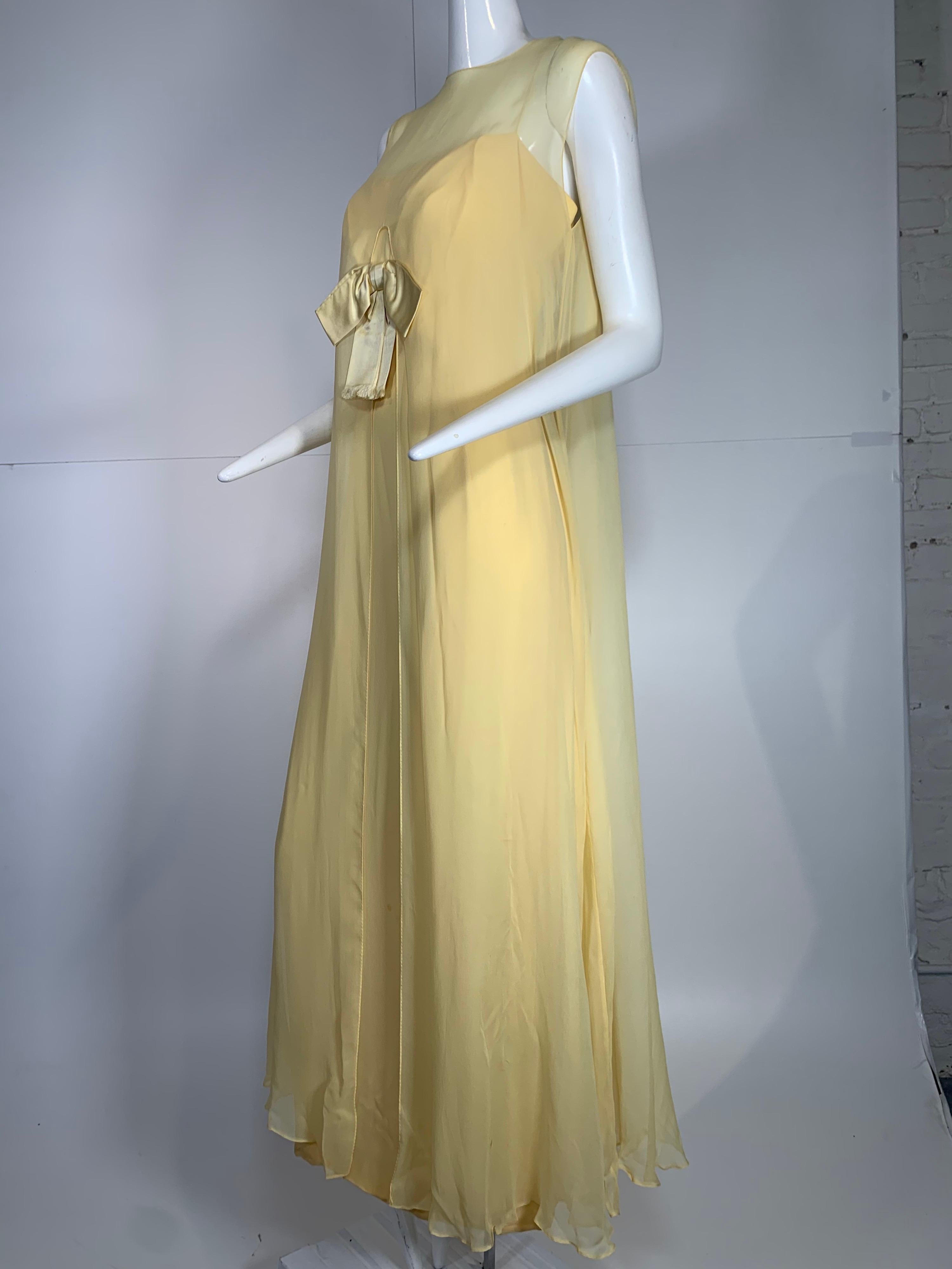 1960er Bonwit Teller blassbuttergelbes Seidenchiffon-Säulenkleid mit Schleife vorne. Separate Overlay-Schicht, die vorne geteilt ist, so dass die Schleife am Mieder des Kleides außerhalb des Overlays sitzt. Reißverschluss an der Rückseite der Säule.