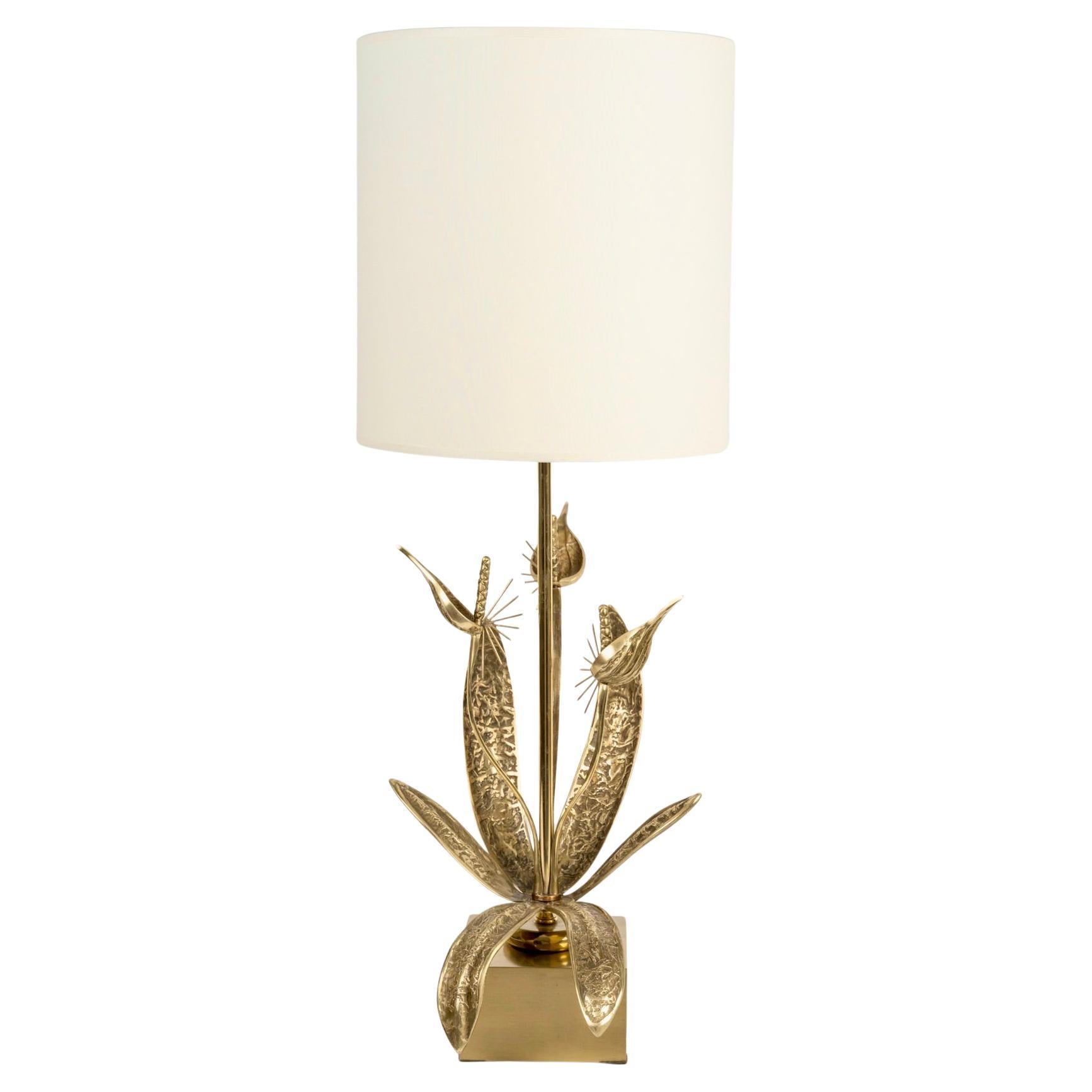 Composto da una base cubica in ottone con patina marrone su cui poggia un alto stelo in ottone dorato decorato alla base con fiori di uccello di paradiso e fogliame in bronzo dorato.
Un paralume cilindrico bianco sporco con la stessa finitura copre