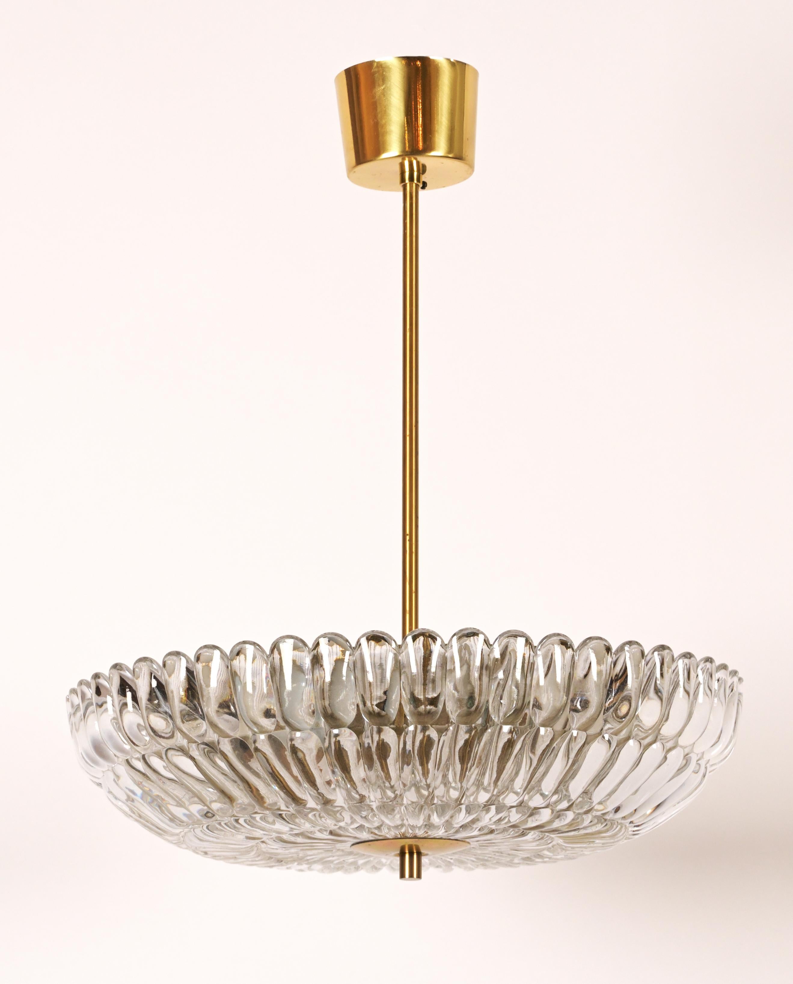 A Swedish Orrefors pendant designed by Carl Fagerlund (1915-2011) A light spun brass frame having over-scaled nail head motif crystal concealing three electric candelabra sockets. The underside with texture glass diffuser secured by finial. The