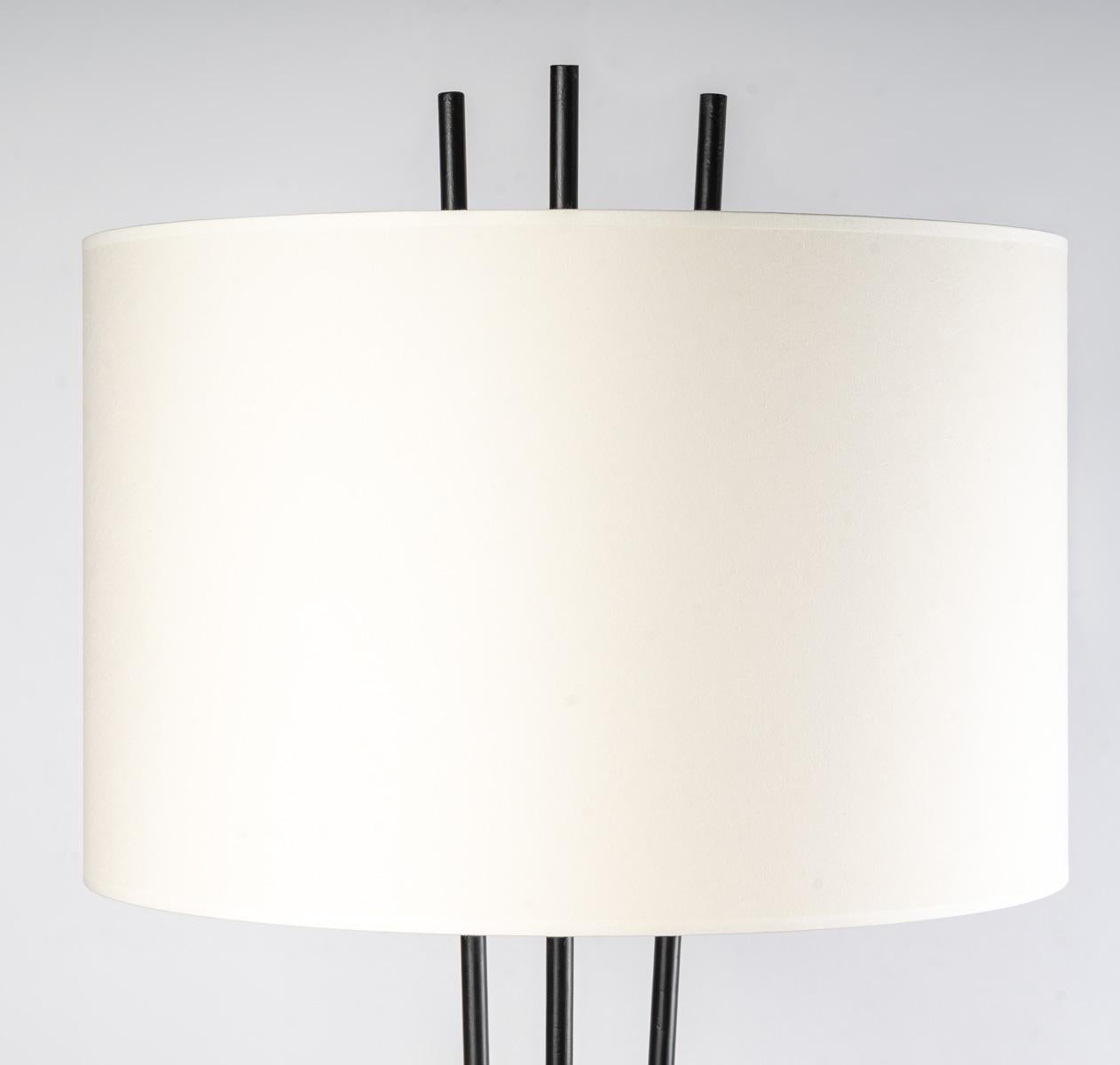 Composed of 3 long vertical rods in black wrought iron opening like a vase.
In the upper part, a large cylindrical lampshade of off-white color (lampshade redone identically) dresses up the floor lamp nicely.

In the lower part, the 3 rods meet and