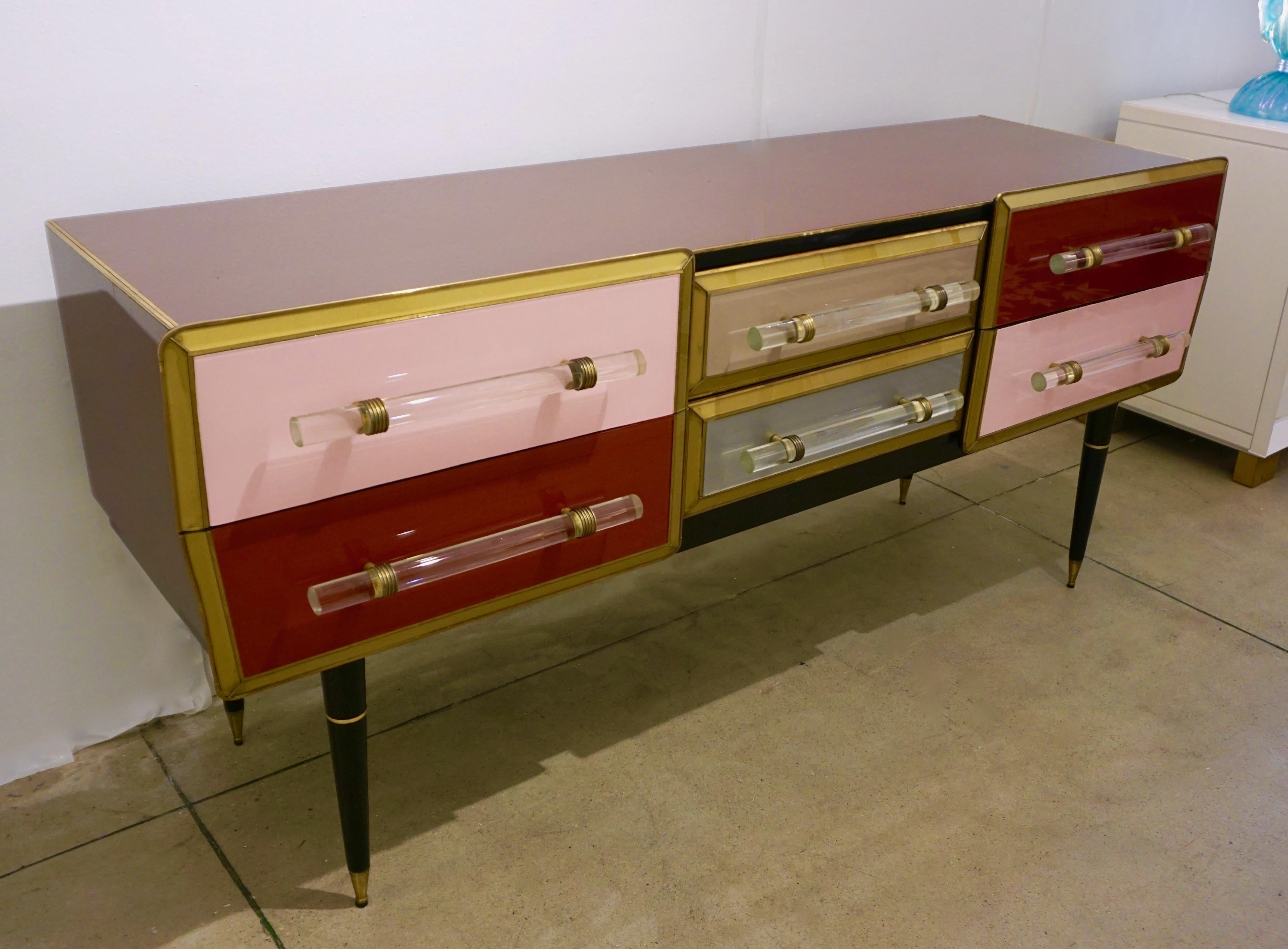 Early 1960s, mid-20th century vintage credenza/chest of drawers, entirely handcrafted in Italy, enticing pop art design with arrow pointed side drawers and rounded corners, the surround covered in glass having unusual color in rich dark red