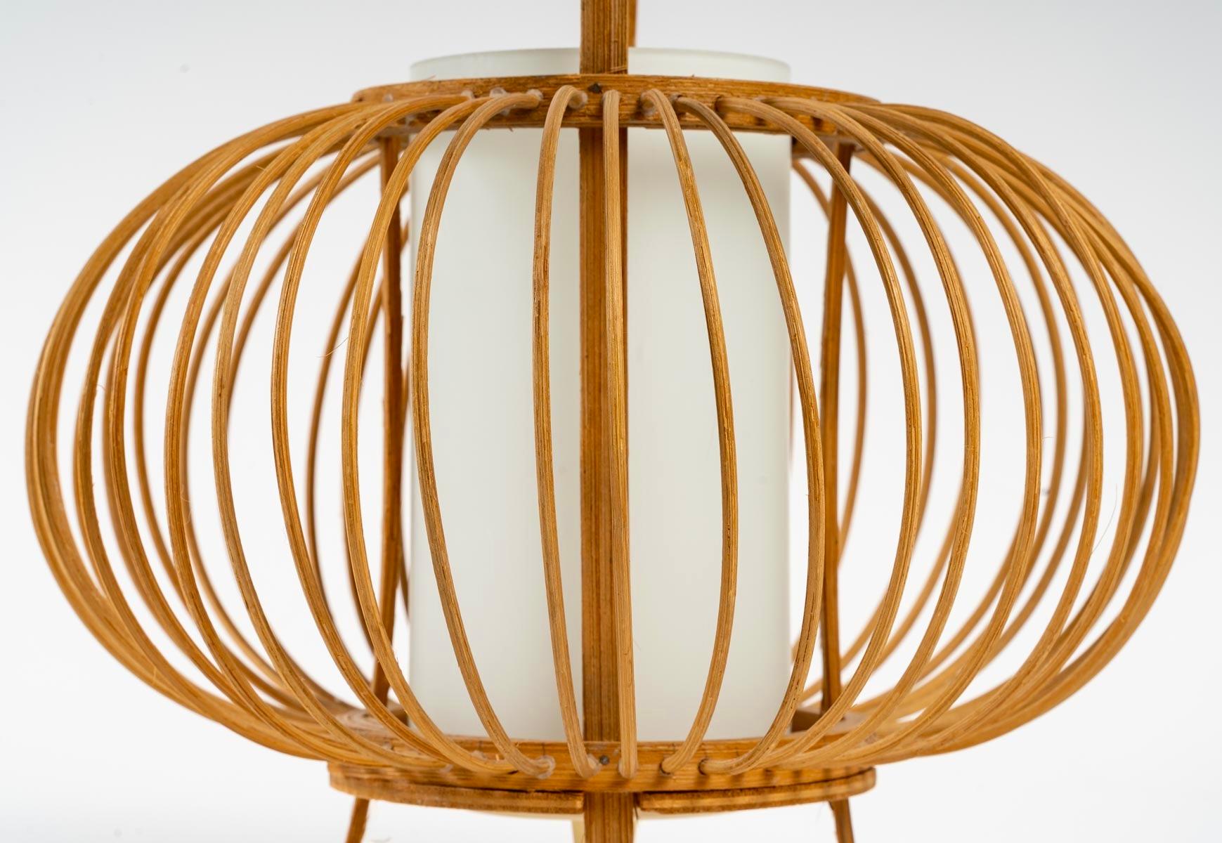 La lampe repose sur quatre petits pieds en bambou sur lesquels est placée une cage ronde composée de deux cercles en bambou en haut et en bas, entre ces deux cercles sont placées de fines tiges de bambou tout autour formant un joli panier dans