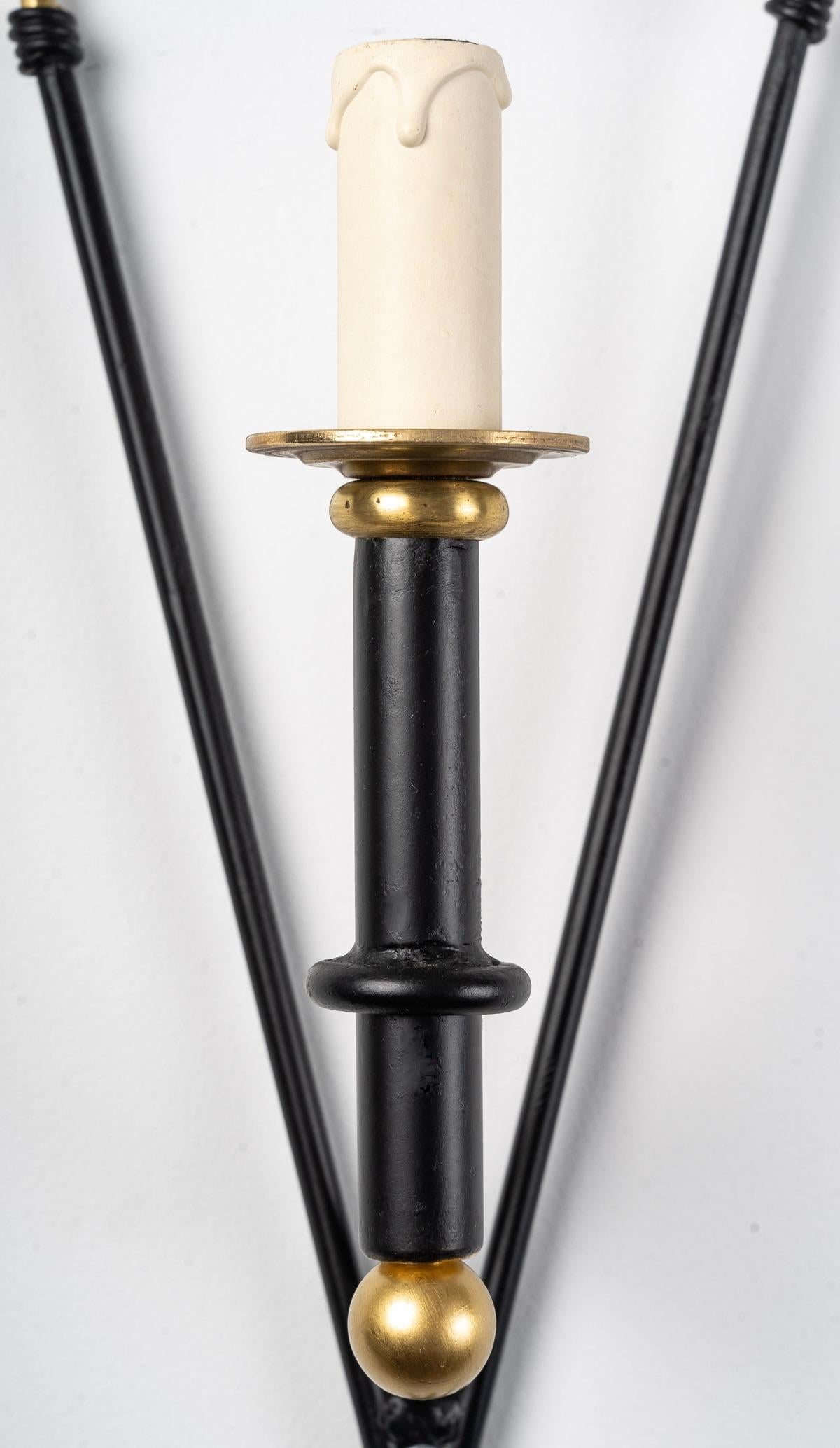 Composed of two black wrought iron arrows decorated with golden feathers, they cross on the lower part.
At the intersection of the arrows, an arm of light placed at the front of the wall lamp is formed by a black wrought iron tube adorned with a