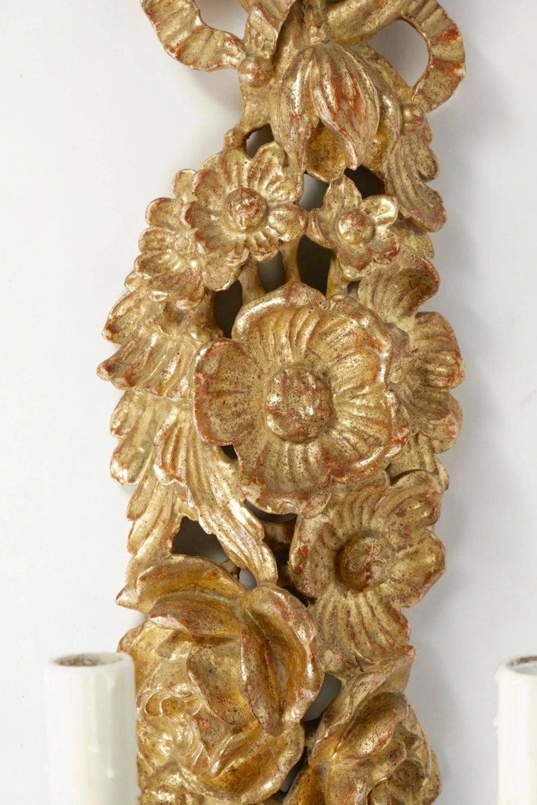 Large pair of sconces from the FlorArt House from 1960.
Composed of a large panel with attributes of flowers and foliage and decorated with a pretty ribbon on the upper part of the sconce in the style of the 18th century.
Two arms of light in gilded