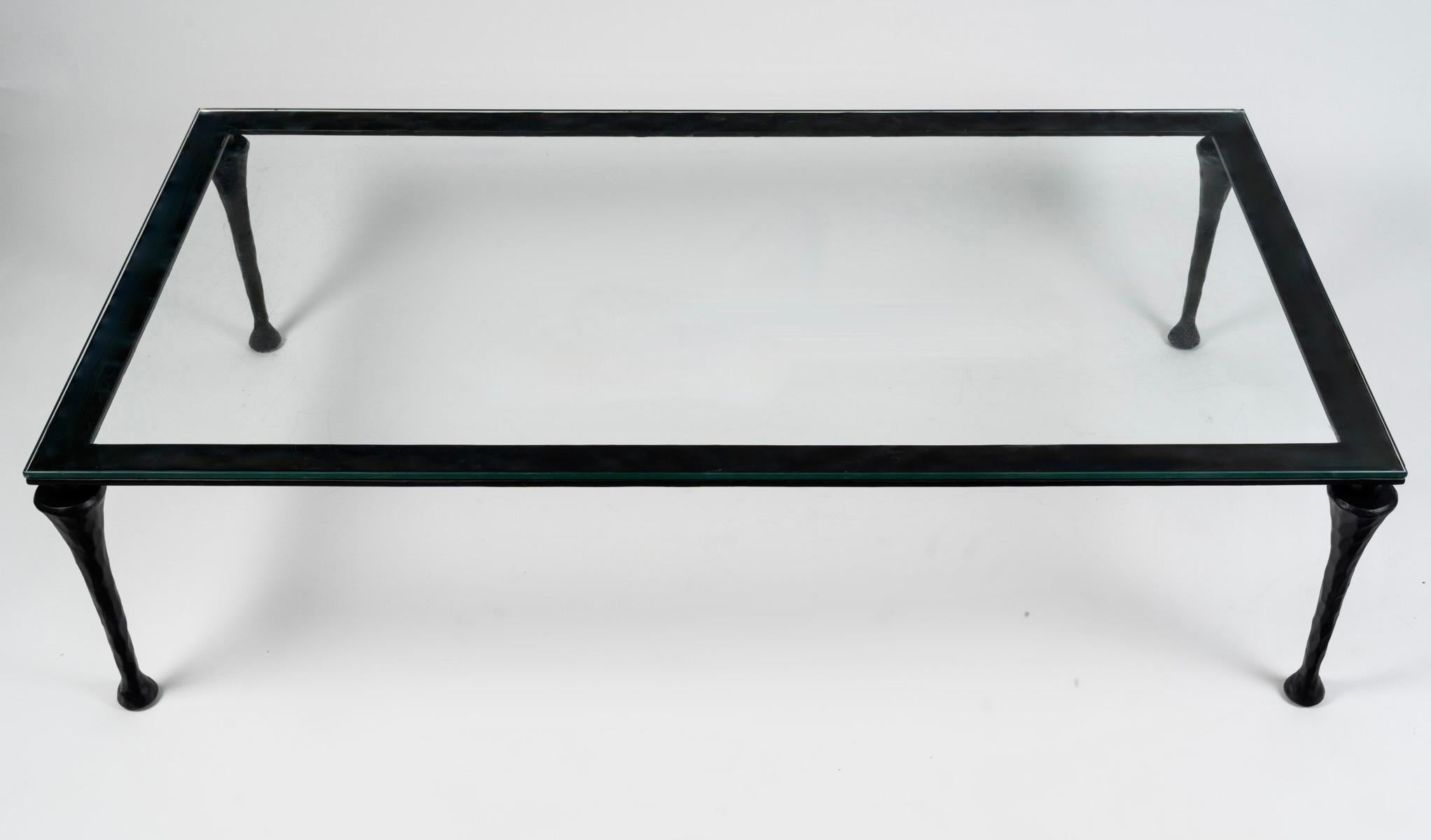 Large wrought iron coffee table by Maison Roche

Composed of a large thick black wrought iron frame resting on four hammered trapezoidal legs ending in shower feet.
The whole piece rests on a large thick glass top polished around the edges.