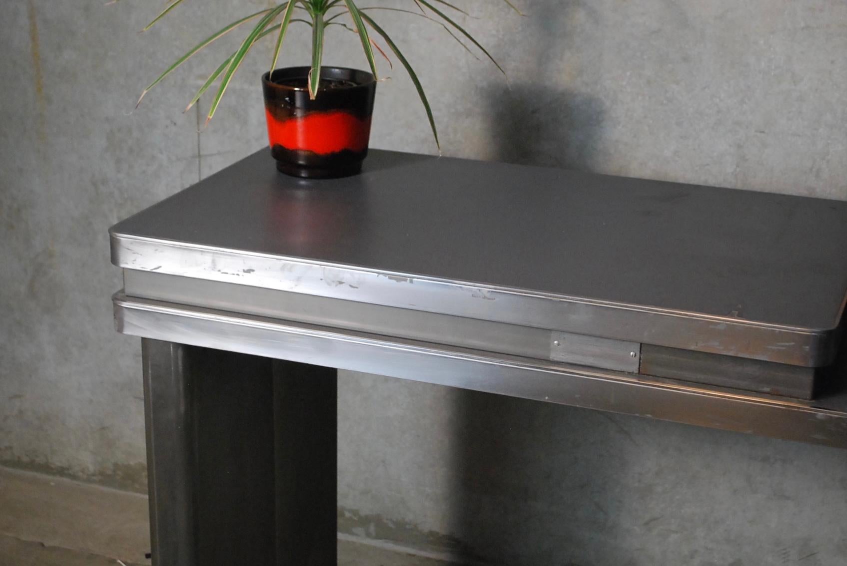 Metal console produced and signed by globe Wernicke with unusual extra top height and adjustable legs.
The legs can move inward or outward depending on use and preference. Solid piece retaining original top and brushed steel finish.