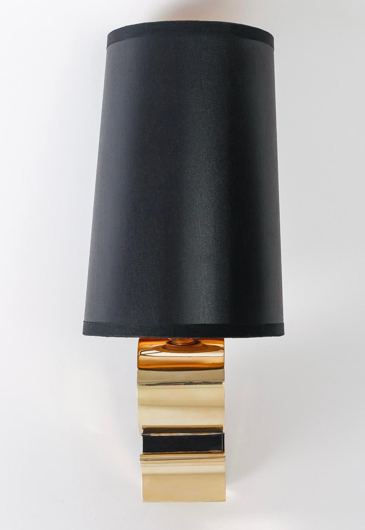 Composed of a rectangular gilded bronze wall bracket on which rests the gilded and blackened bronze baluster-shaped light arm.
The top of the baluster is adorned with a trapezoidal lampshade in black cotton on the outside and gilded on the