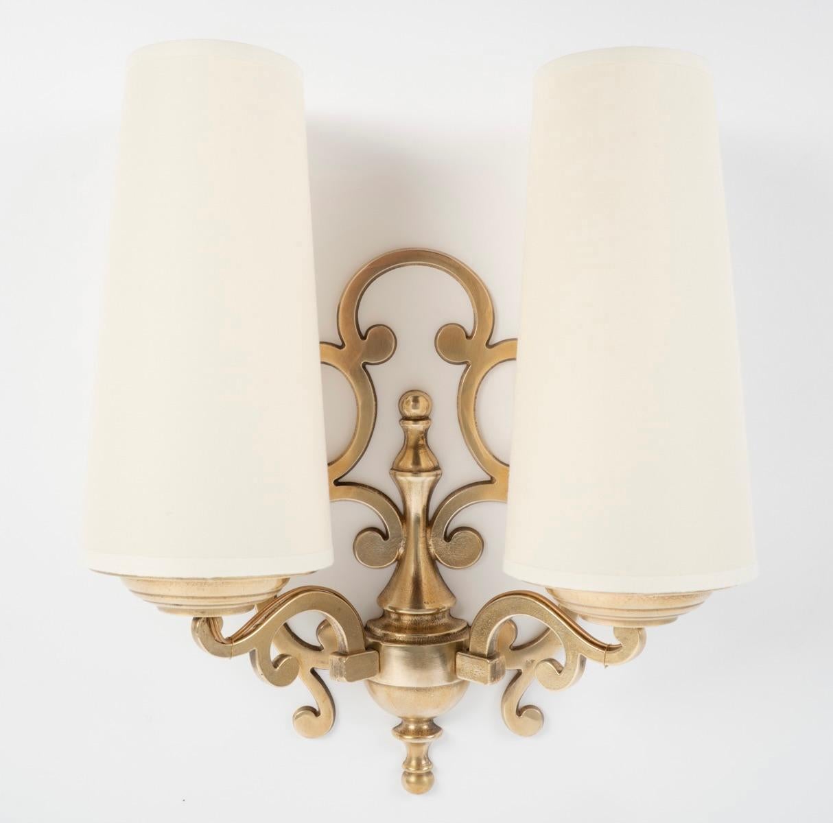 Whiting comprend une grande plaque murale décorée de rinceaux, sur laquelle reposent deux bras de lumière orientés vers le haut, également décorés de rinceaux et dotés de deux abat-jour coniques identiques en coton blanc cassé. L'ensemble de la